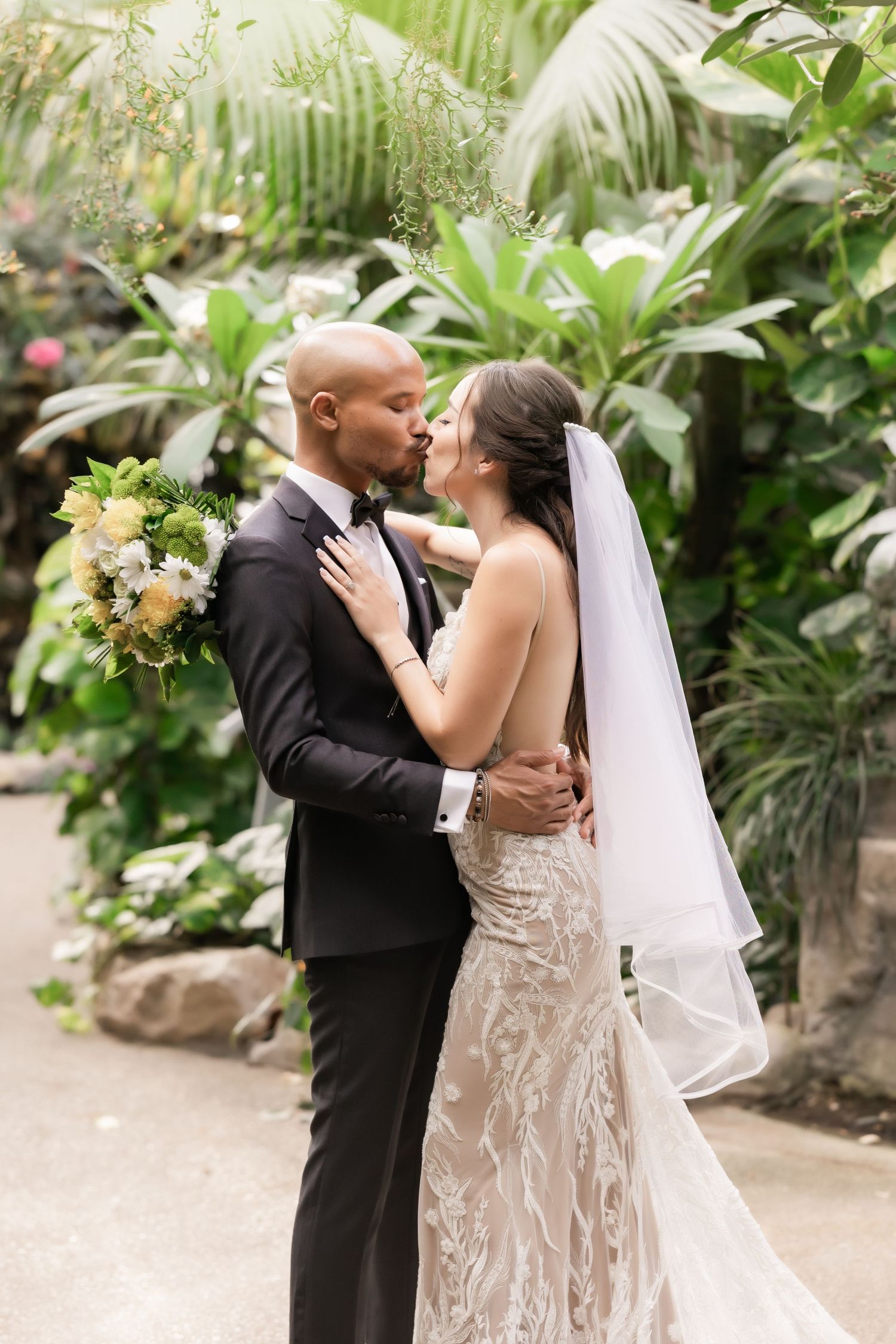 Intimate wedding portrait of a couple embracing in front of tropical foliage and greenery.