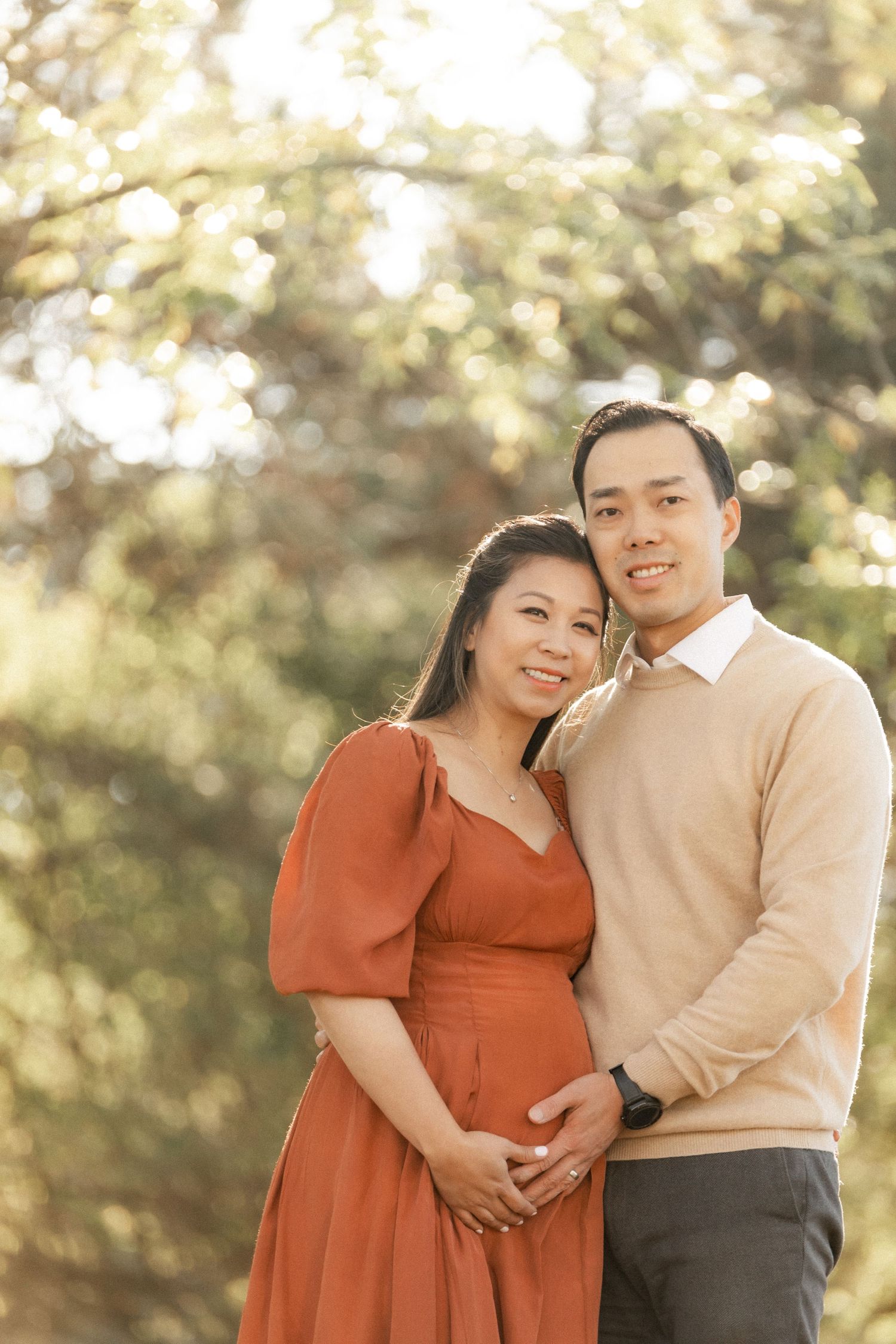 A maternity portrait featuring a couple in coordinating rust and beige outfits against a natural background.