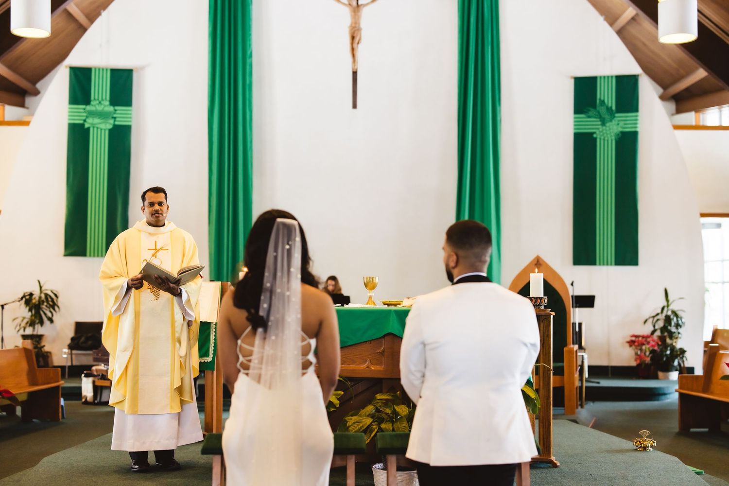 A Catholic wedding ceremony taking place in a church with green banners and a central crucifix.