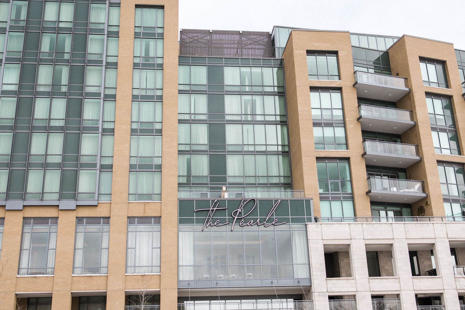 Modern apartment building exterior with glass balconies and tan accents.