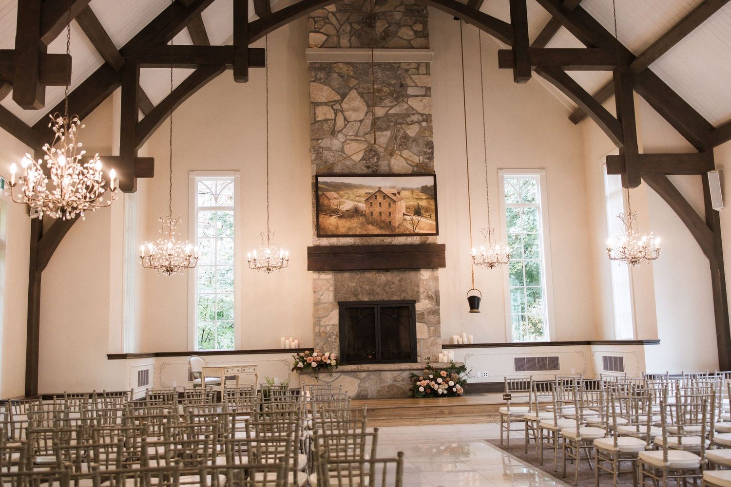 Elegant wedding chapel interior with vaulted ceiling, stone fireplace, chandeliers and rows of white chairs.