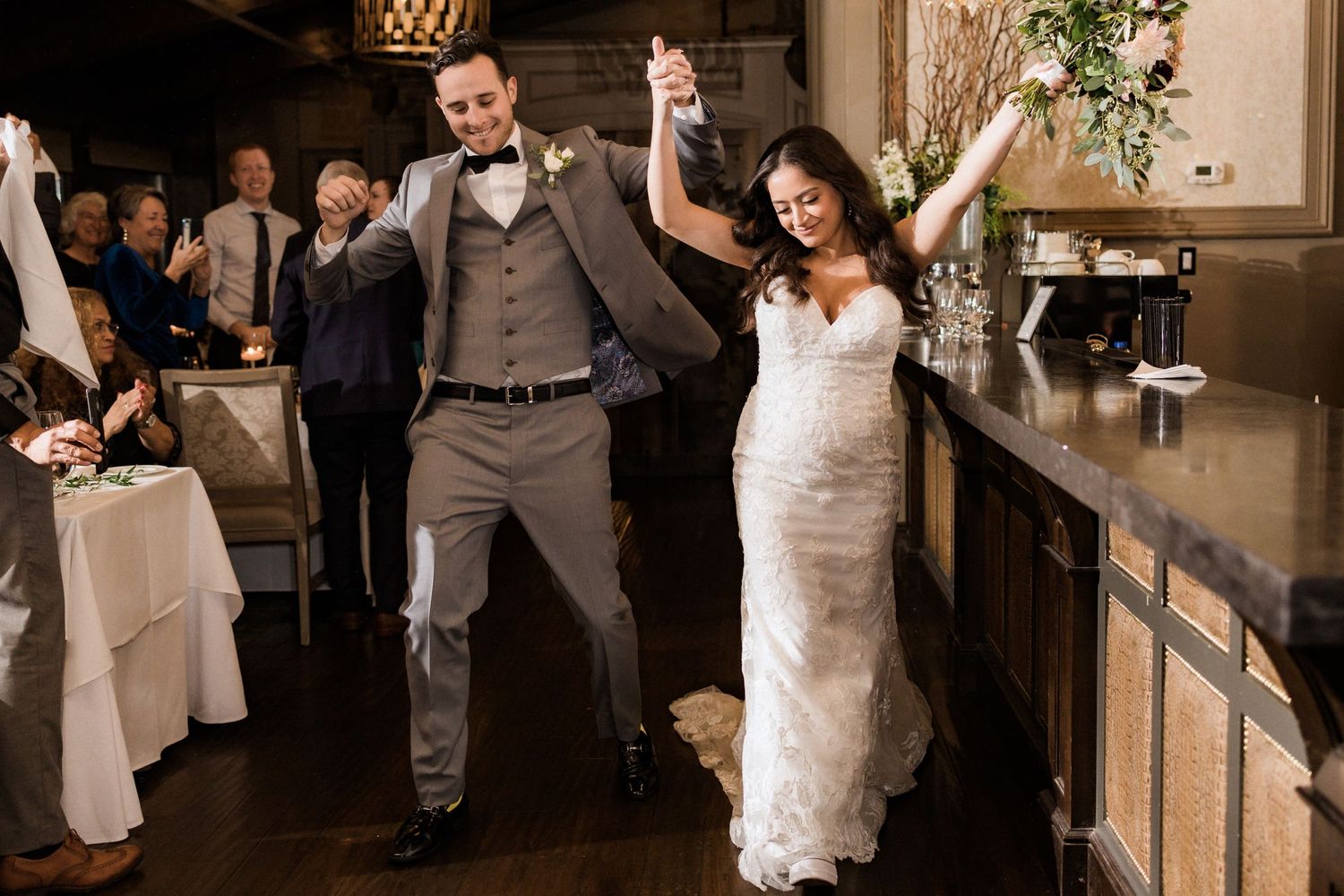 Celebratory moment of newlyweds dancing with raised arms at indoor reception.