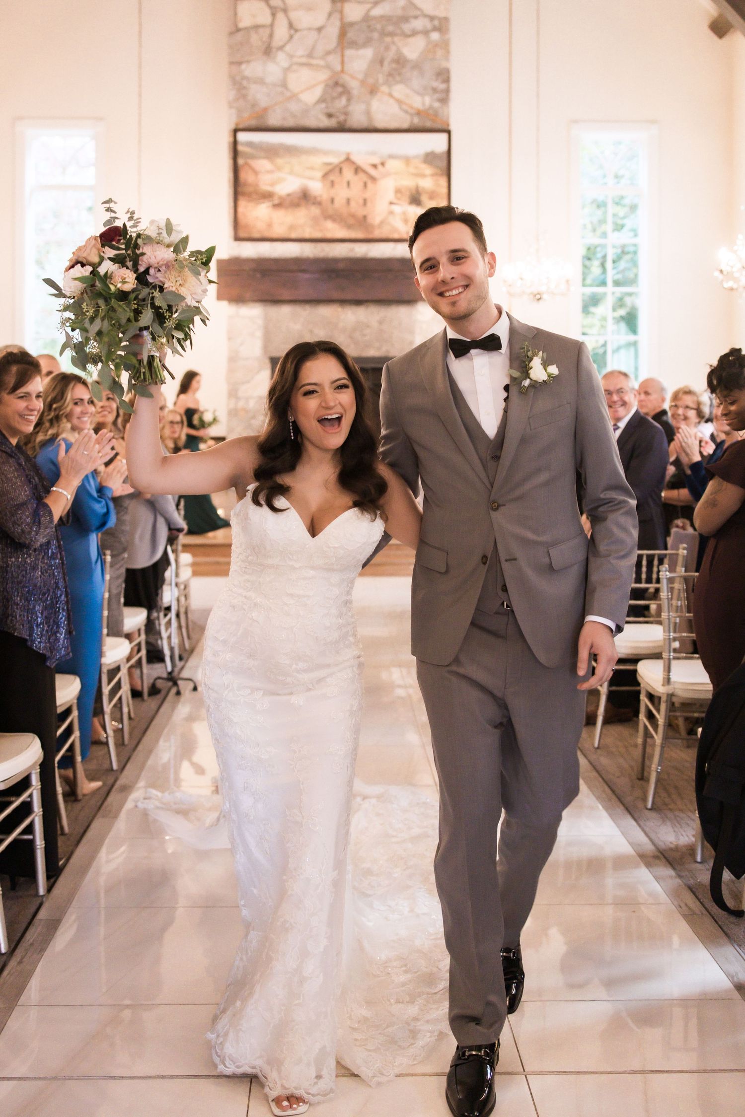 Joyful wedding recessional down white marble aisle with stone fireplace and cheering guests.