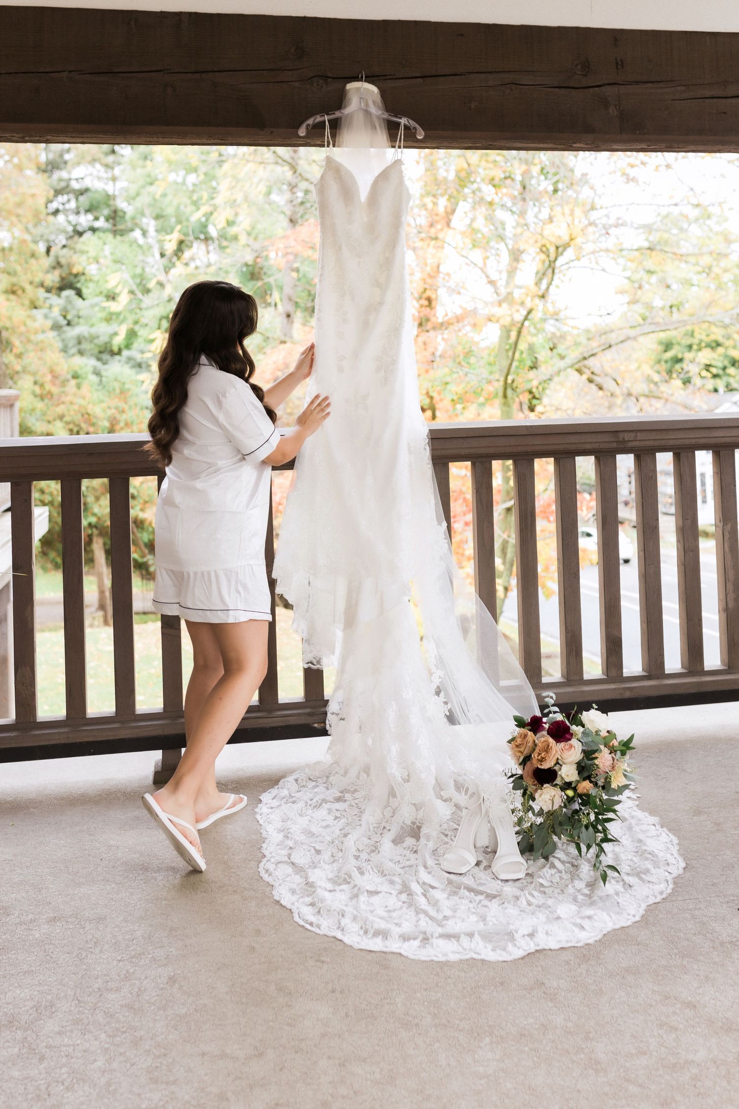 Wedding dress preparation moment on porch with floral bouquet on display.