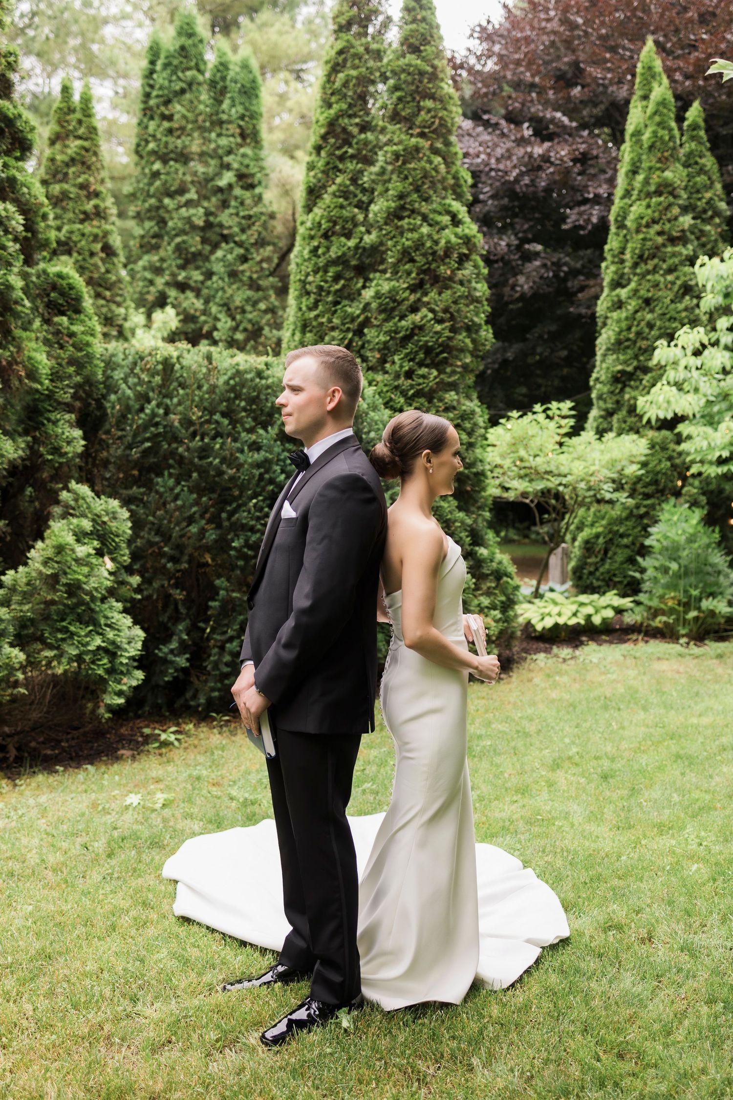 A couple in formal wedding attire share a light moment together in a lush garden setting.