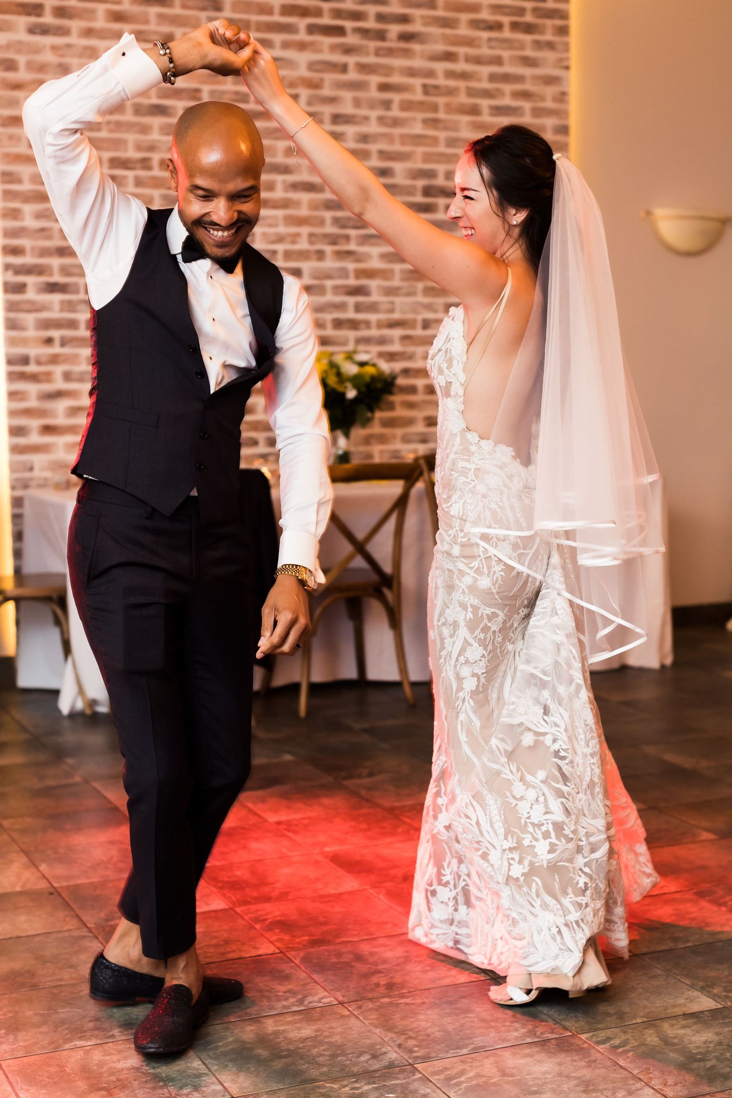 Newlyweds share a joyful dance together at their wedding reception on a red-tiled floor.