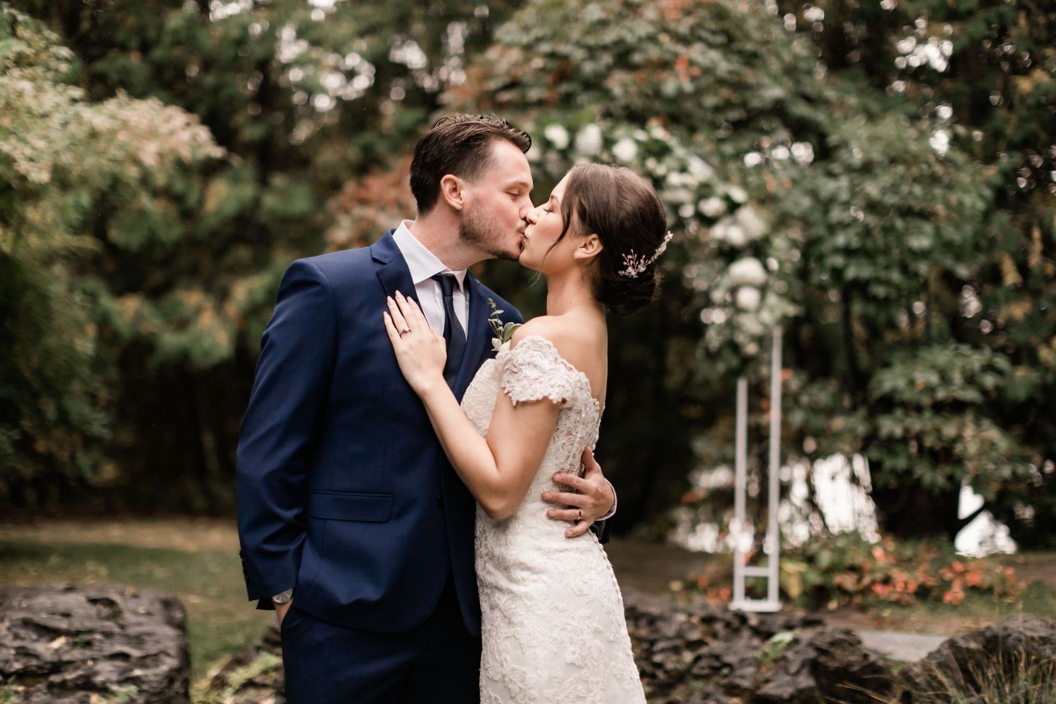 A tender moment between newlyweds sharing a kiss in a garden setting.