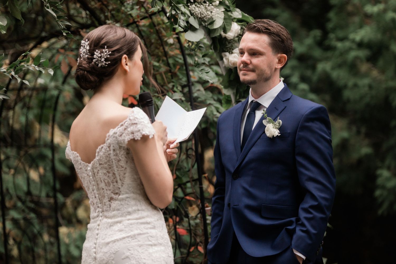 A bride in lace reads her vows to her groom during an intimate garden ceremony.