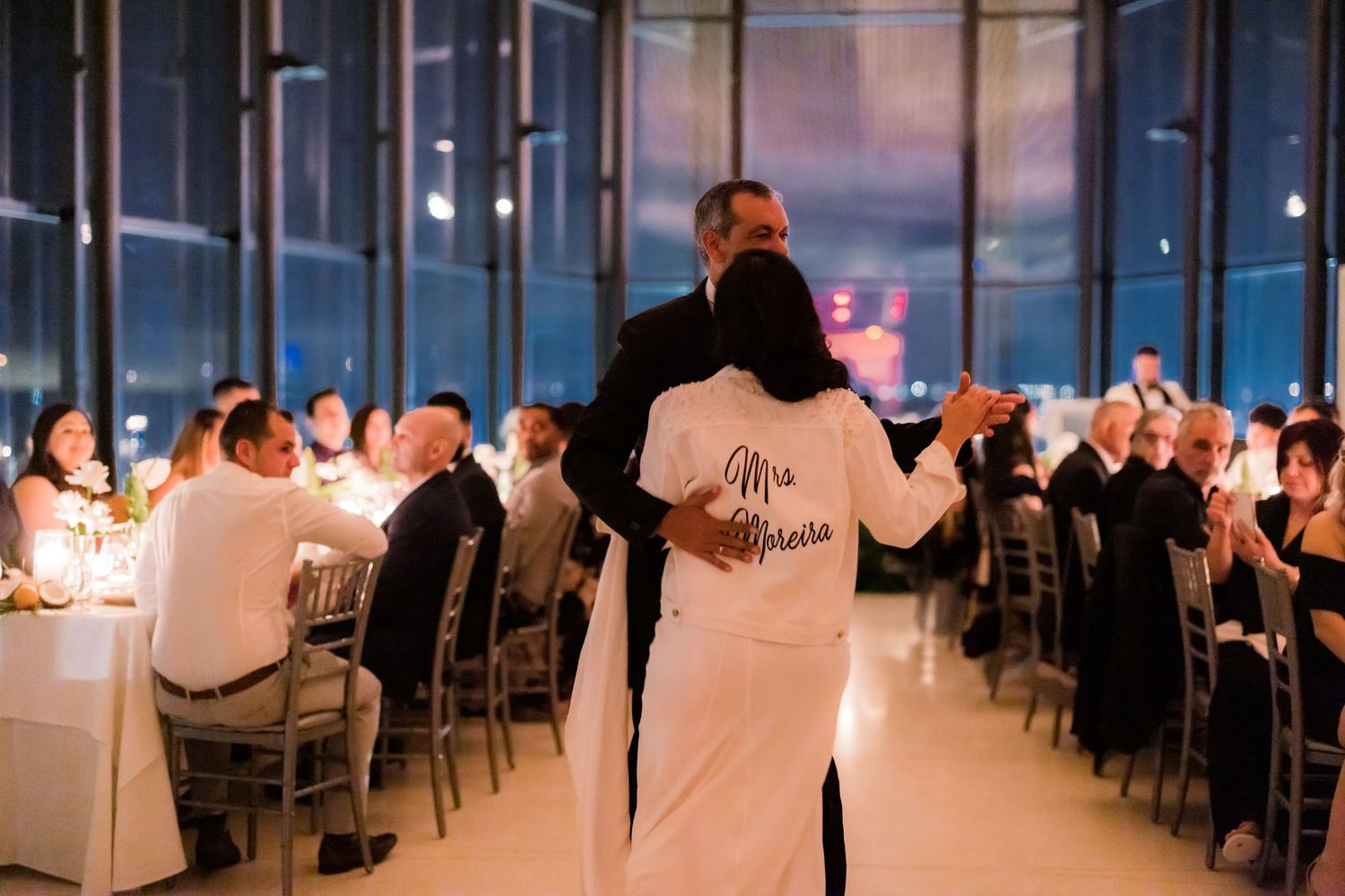 A couple shares their first dance at an elegant candlelit reception with guests seated at long tables.