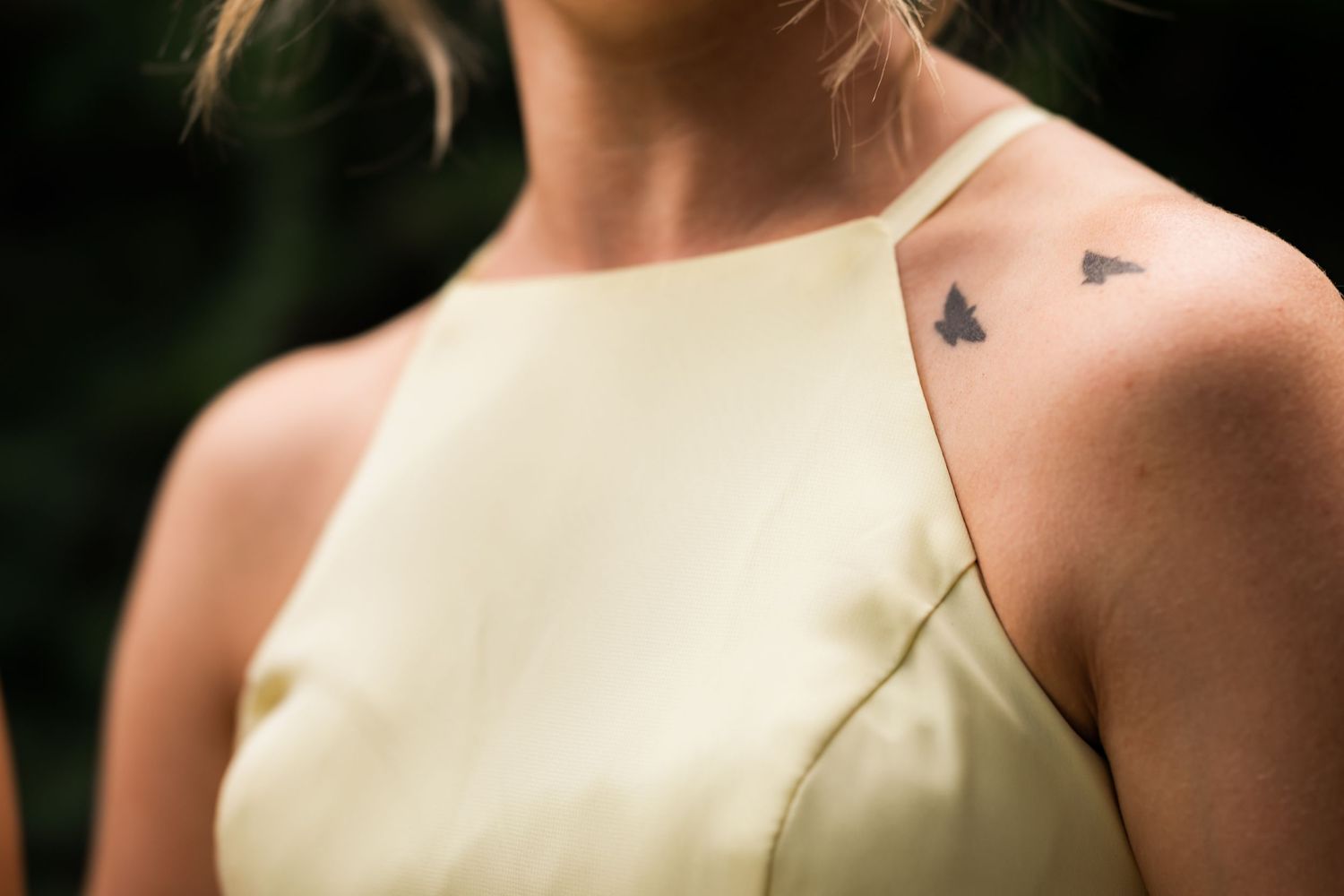 Close-up detail of small heart tattoos on bridesmaid's shoulder in yellow dress.