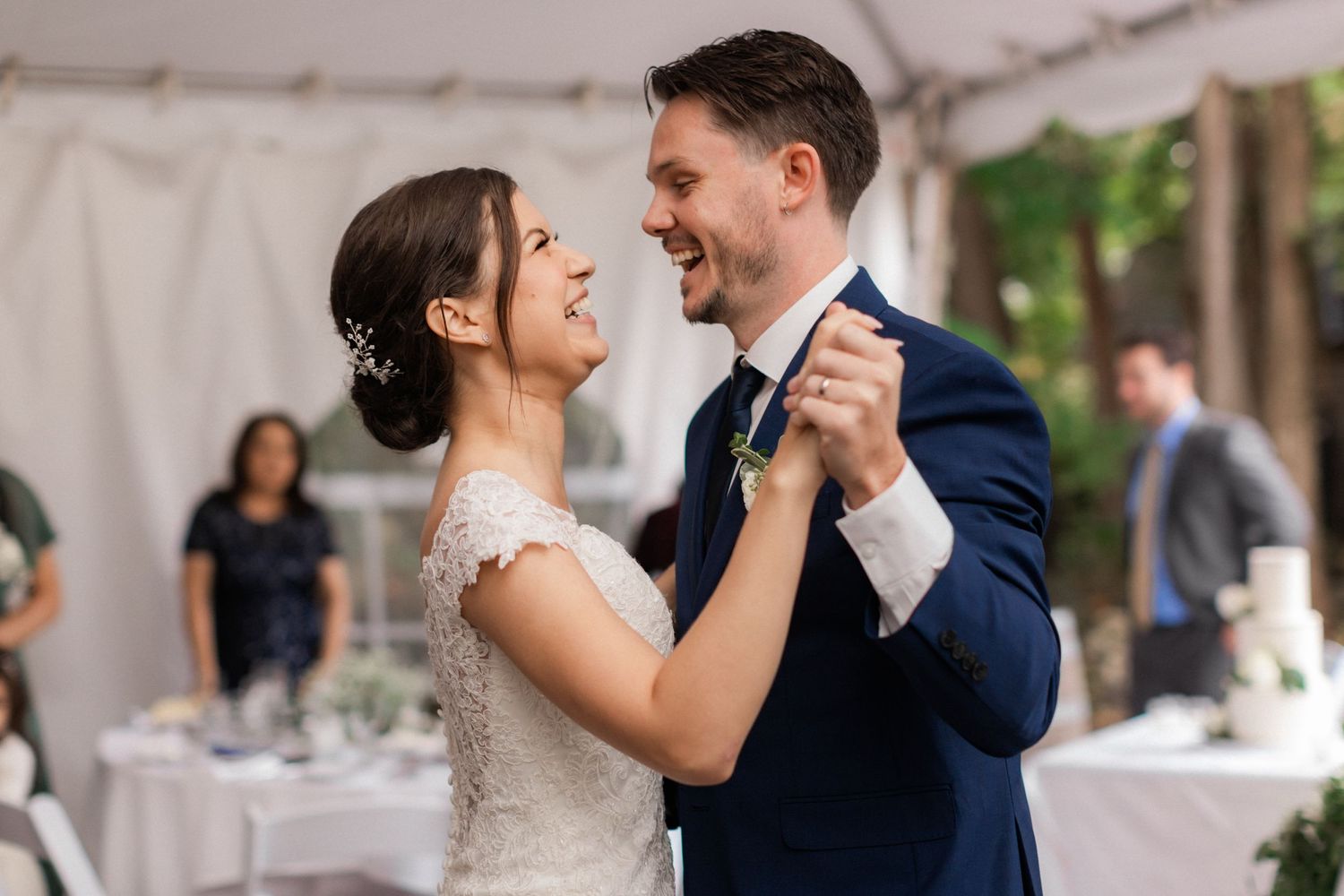 Couple shares their first dance under a white tent at an outdoor wedding reception.