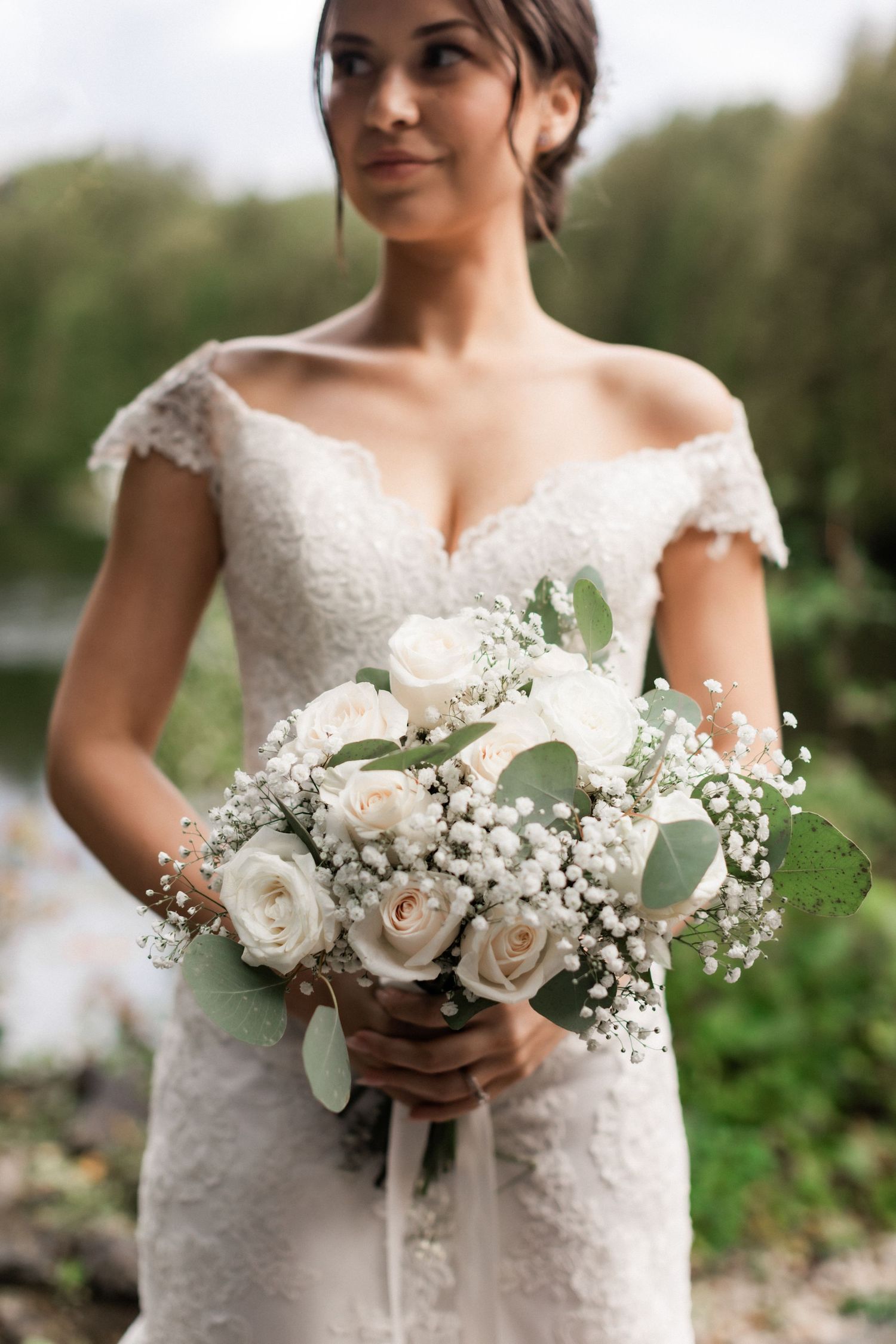 A bride in lace holds a stunning white rose and baby's breath bouquet.