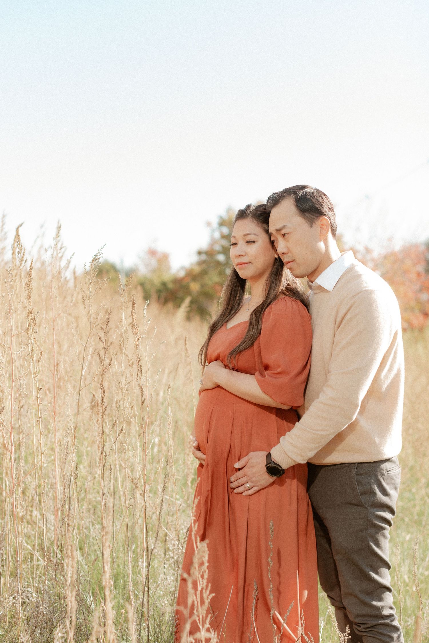 A couple embraces in a sun-drenched field of wheat during a maternity photoshoot.