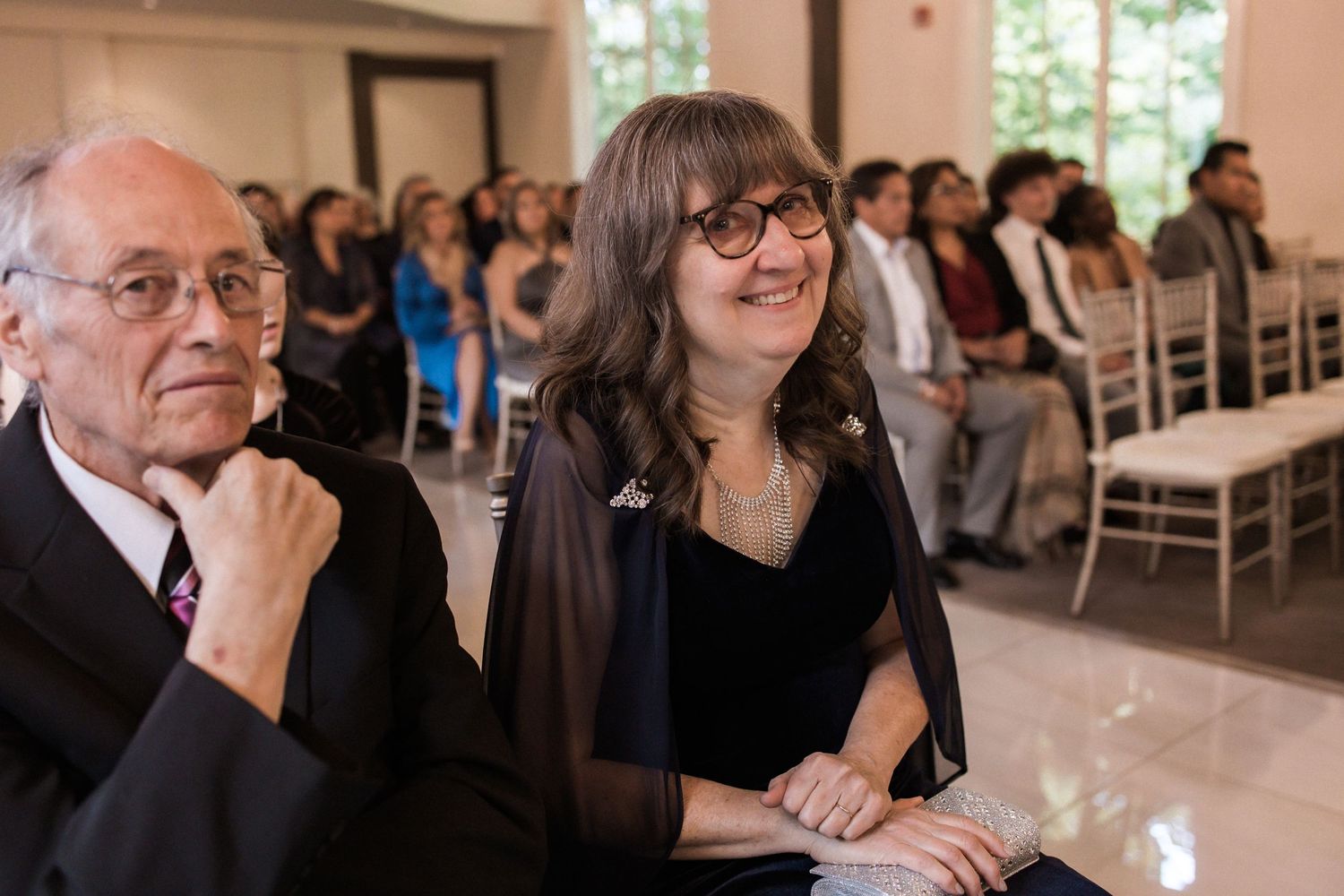 Wedding guests seated in white chairs watching the ceremony in an elegant venue.