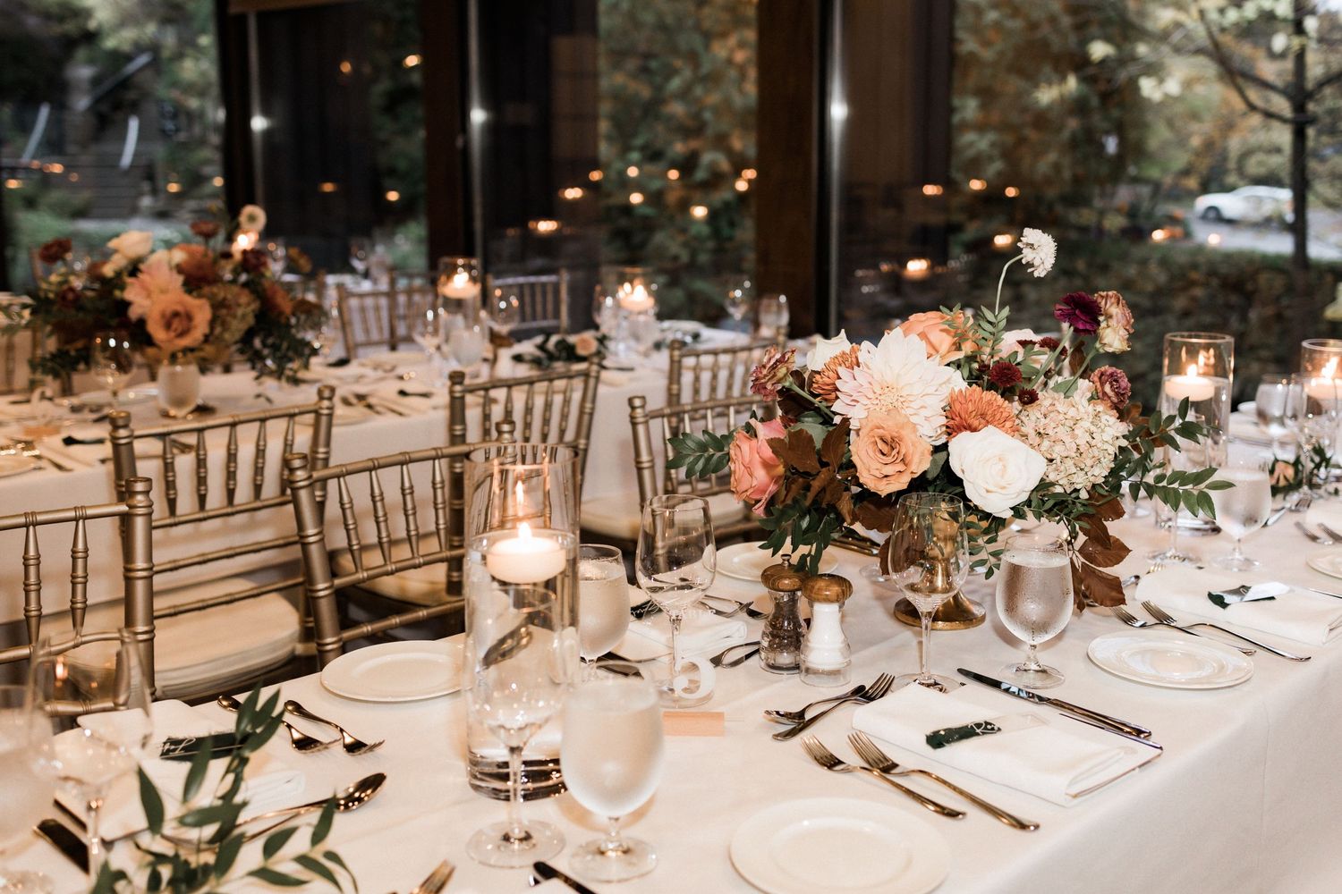 Elegant wedding reception table setting with floral centerpieces, candles, and chiavari chairs.