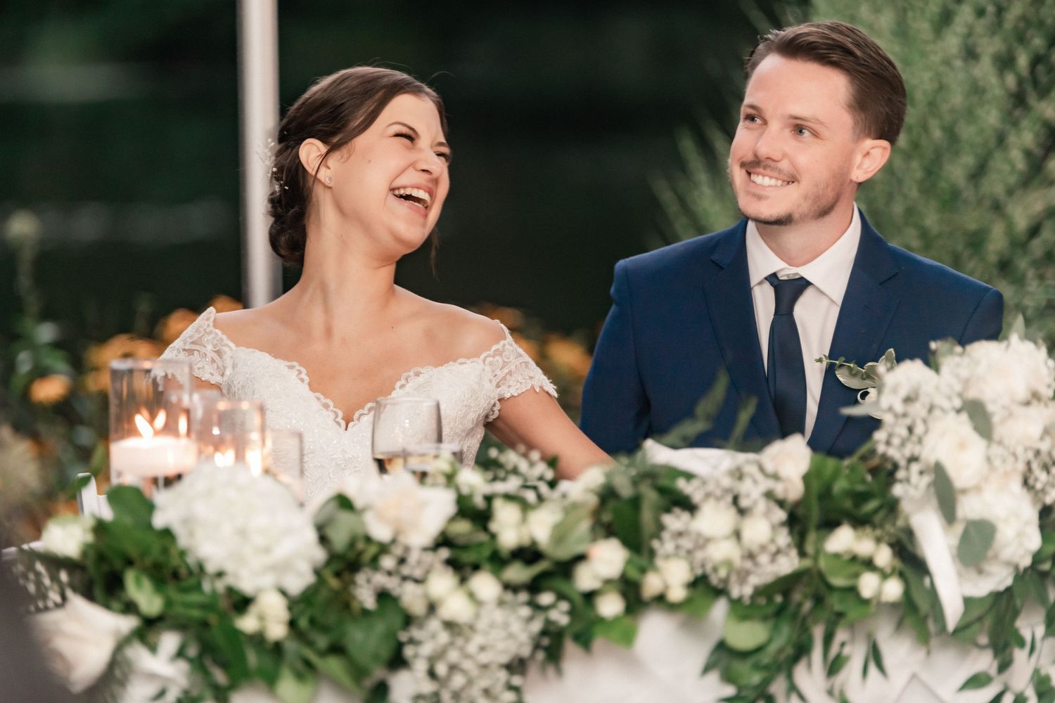 A candid reception moment showing genuine laughter at a wedding table decorated with white flowers.