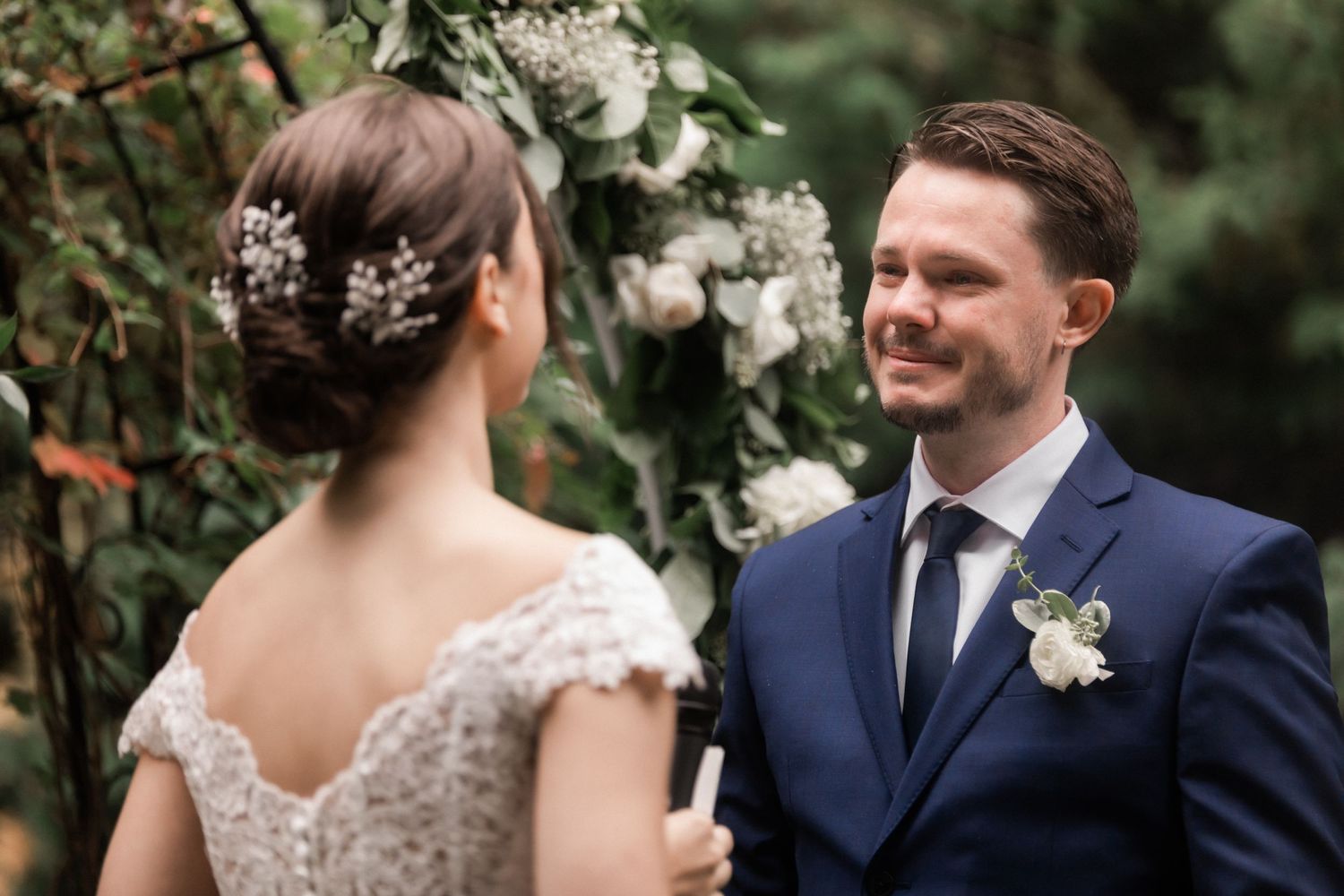 Couple sharing intimate moment at reception table with wine glasses in garden setting.