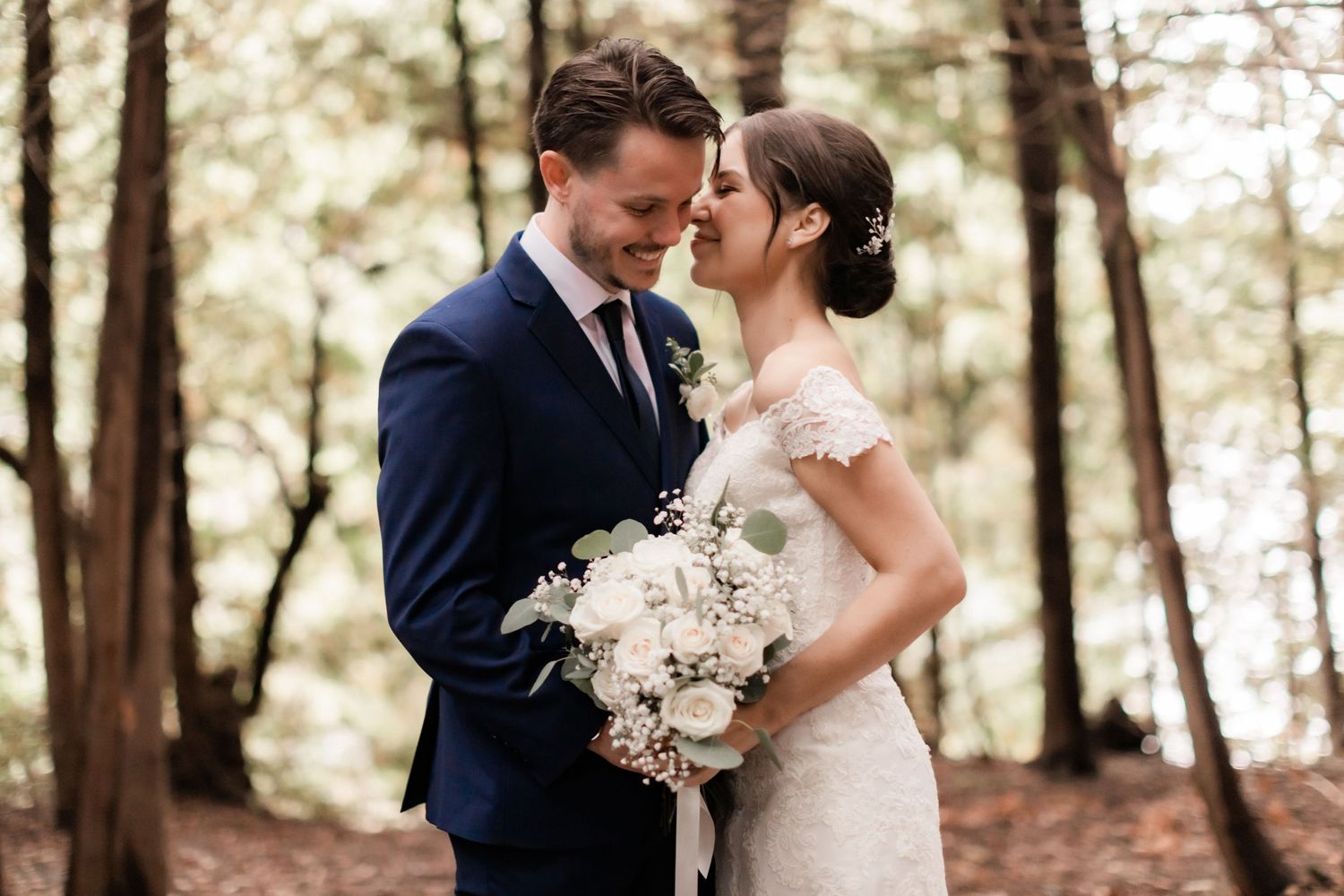 A romantic outdoor wedding photo in a forest setting with white floral bouquet.