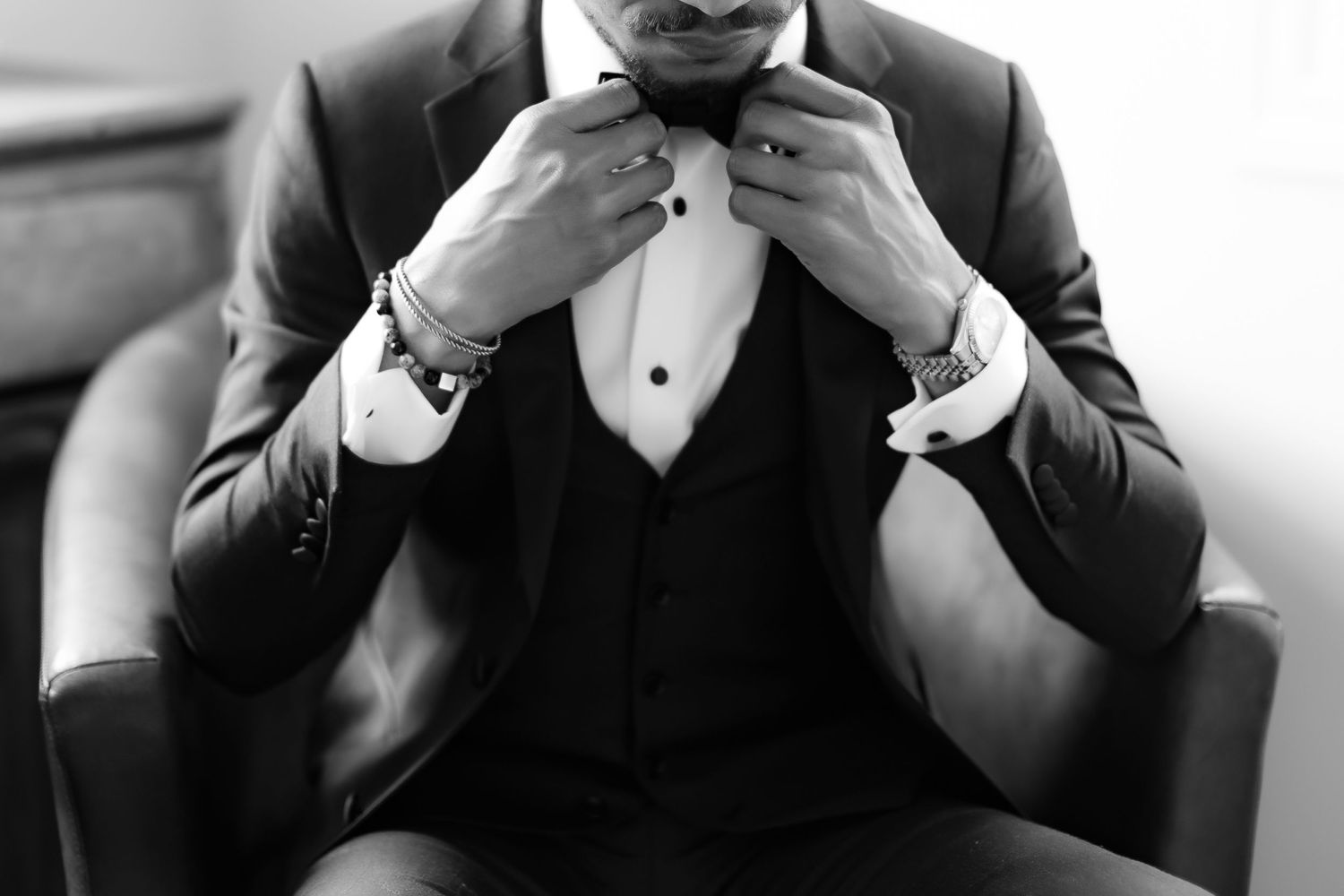 Black and white shot of person adjusting bow tie while seated in formal wear.