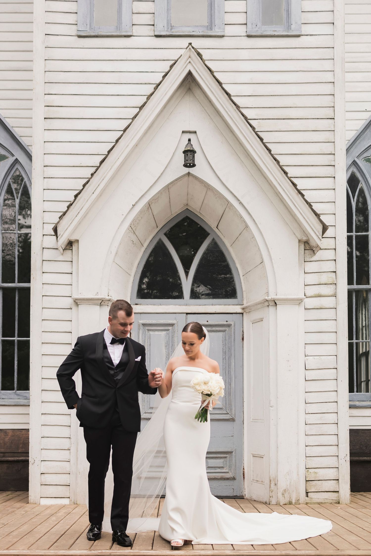 Classic church wedding portrait with couple standing under white gothic archway entrance.