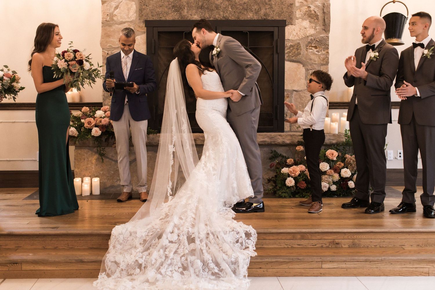 A romantic first kiss at the altar surrounded by elegant floral arrangements and wedding party members.