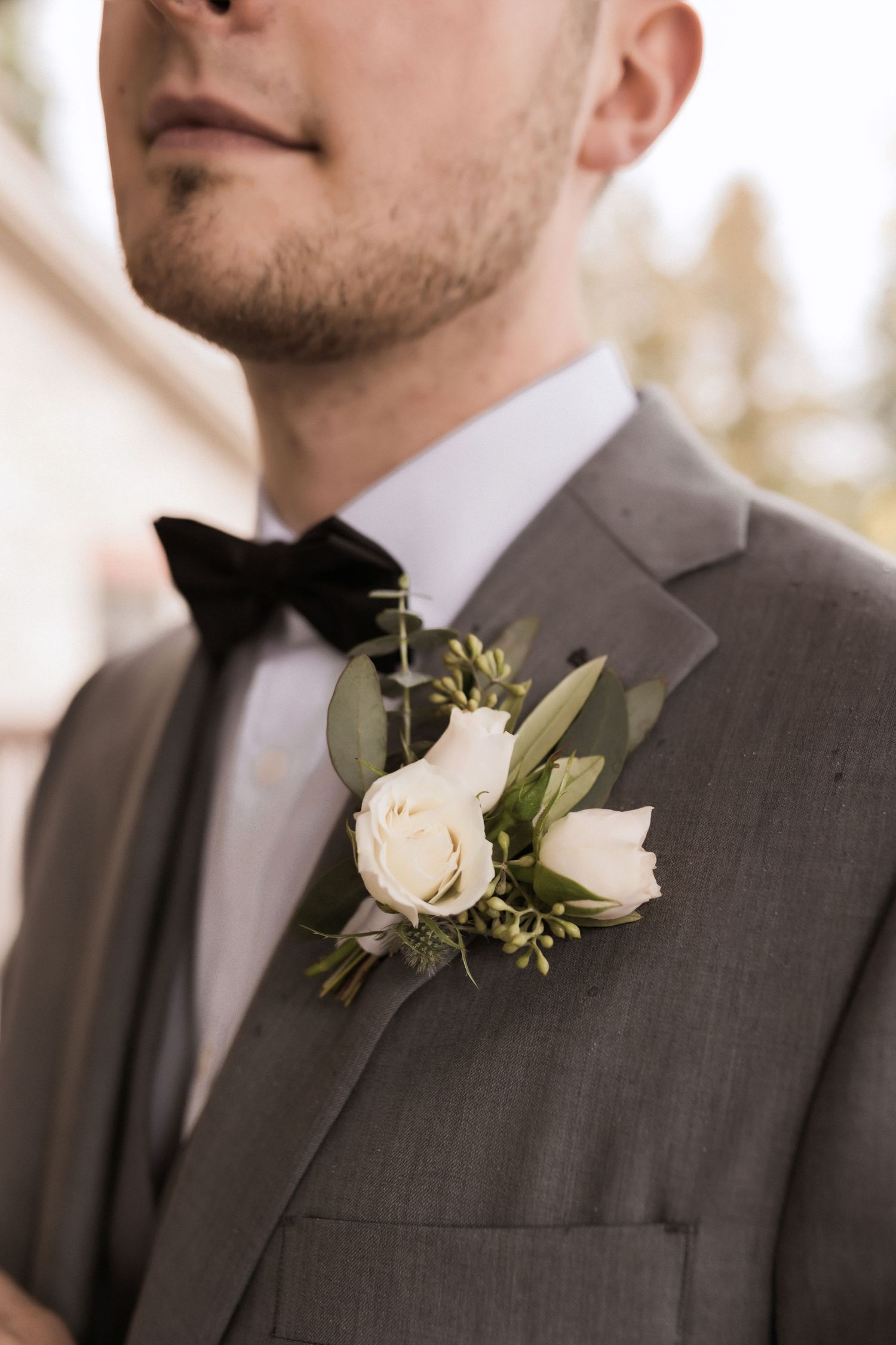 Detailed shot of black bow tie and white rose boutonniere on gray suit jacket.