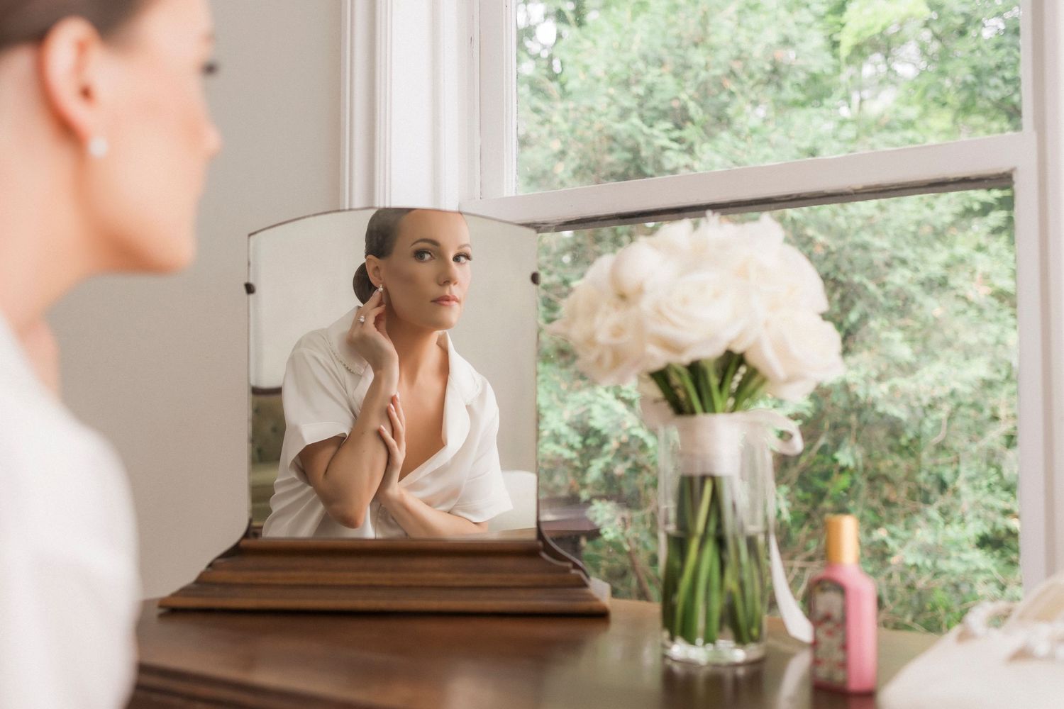 Reflection in mirror on dresser with fresh white peony bouquet in vase and window view.