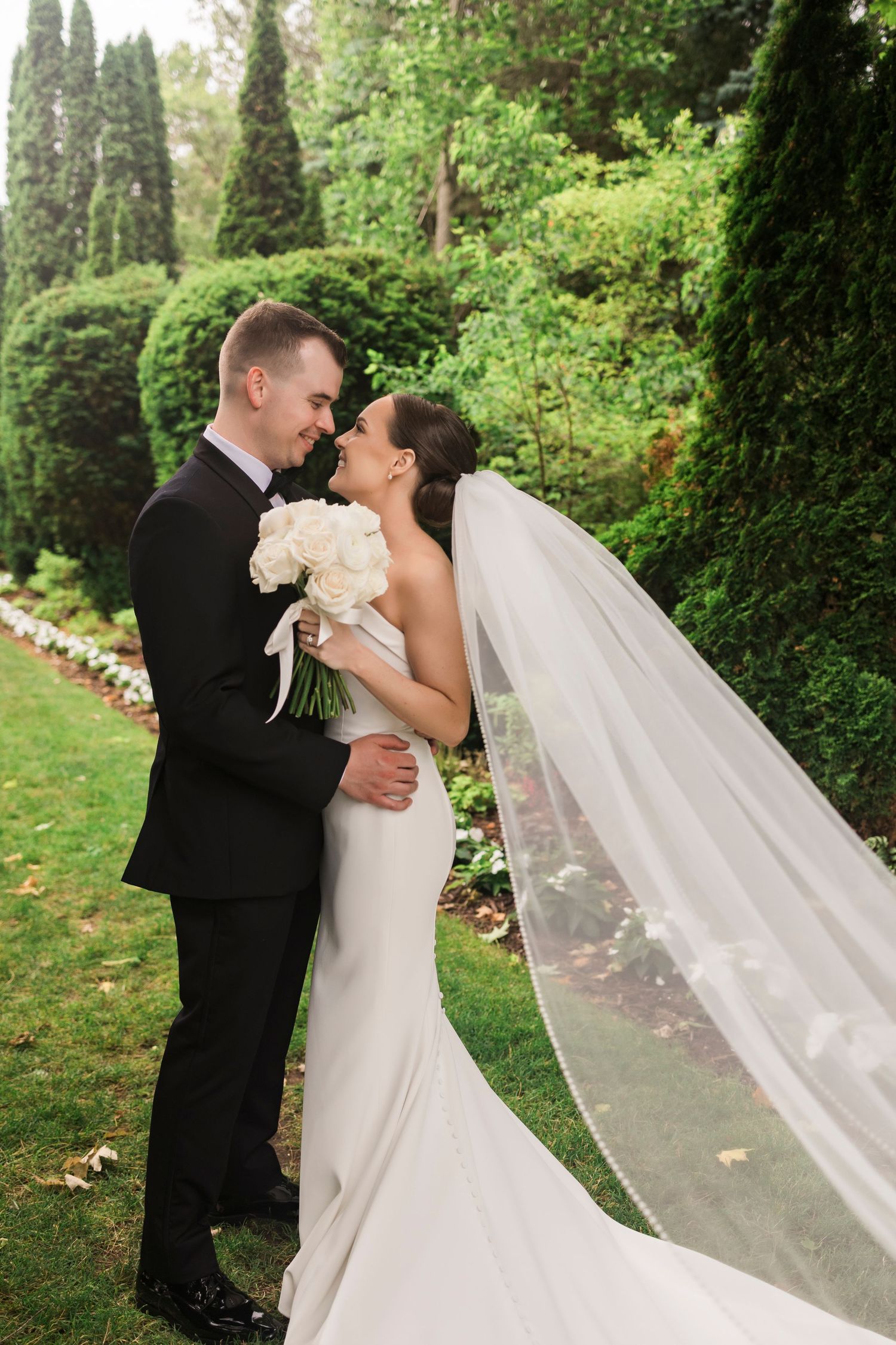 A romantic wedding couple shares kisses in a lush garden setting with flowing white veil.