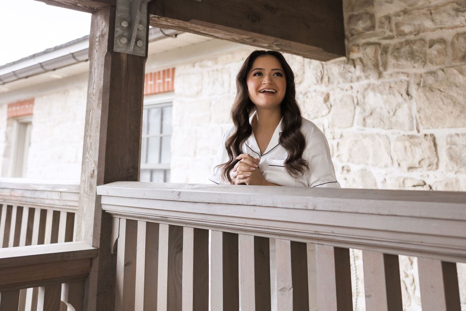 A person in white attire smiling while standing on a rustic stone porch.