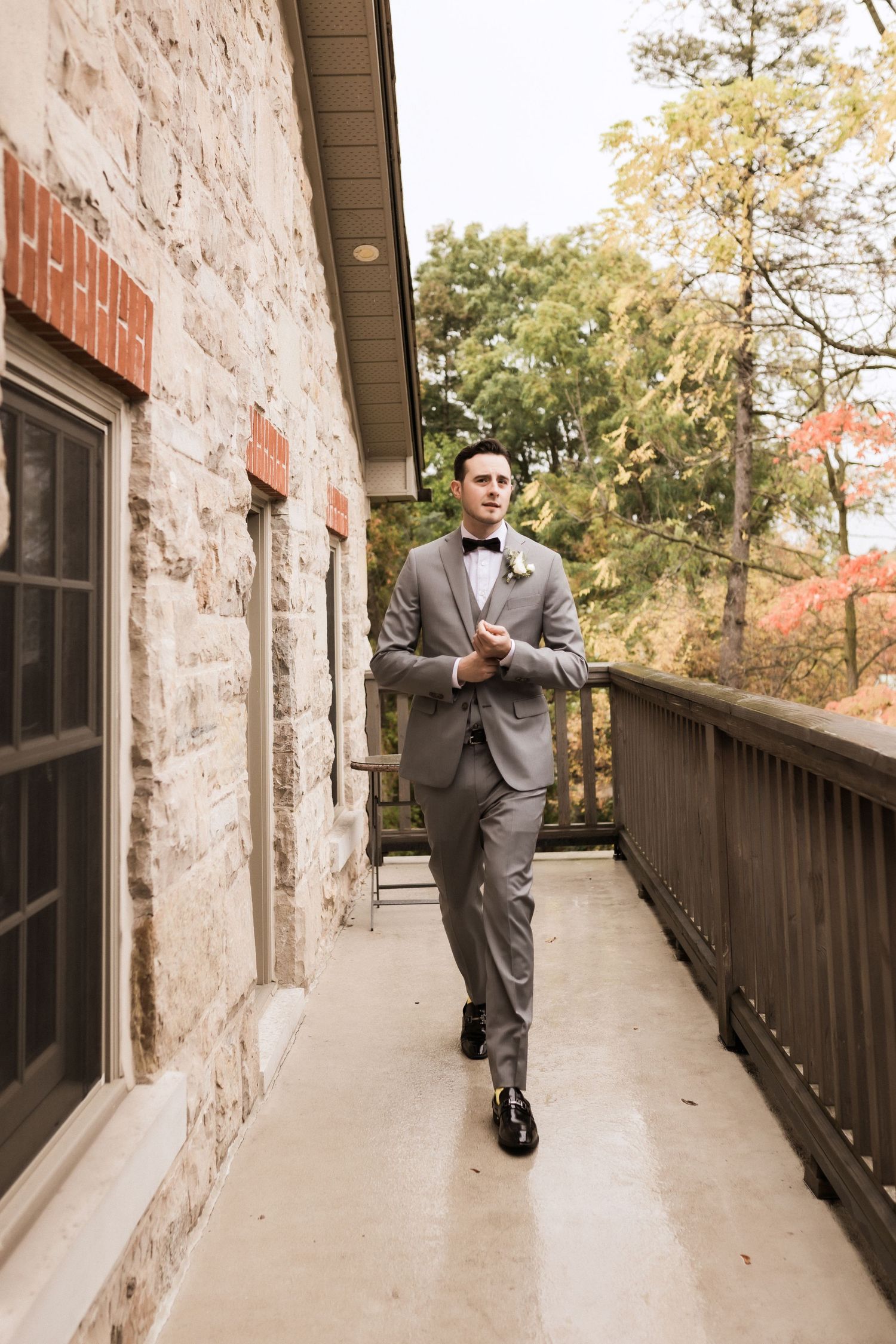 Groom walks along stone building walkway in fitted grey suit.