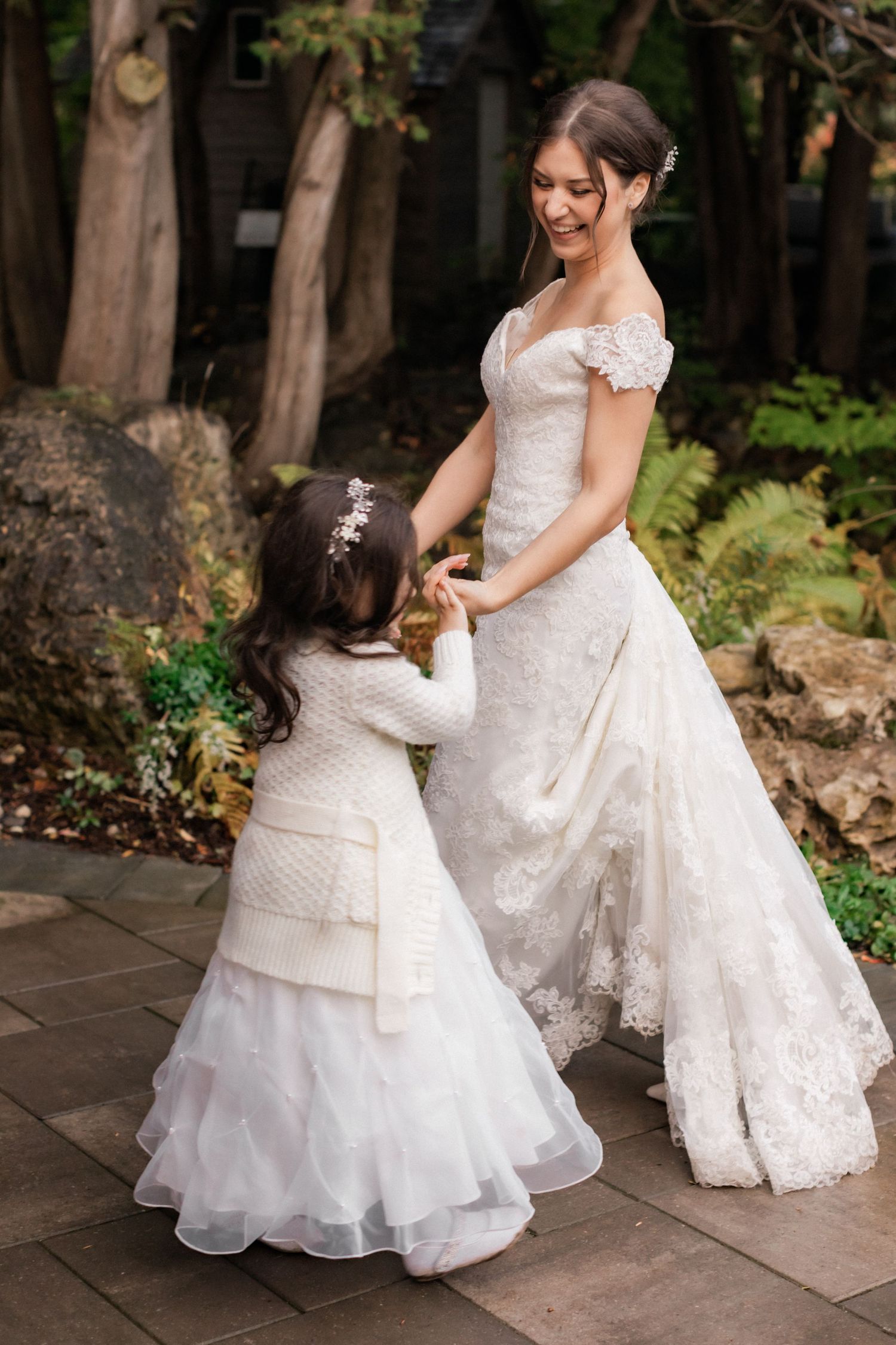 A sweet interaction between a bride and young flower girl both wearing elegant white dresses.