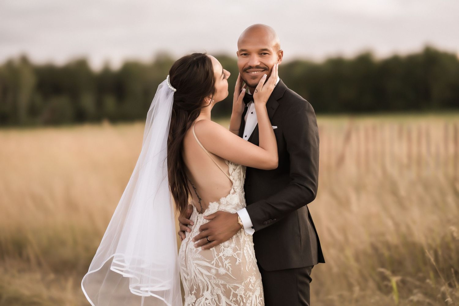 Tender moment between newlyweds in a rustic field setting during golden hour.