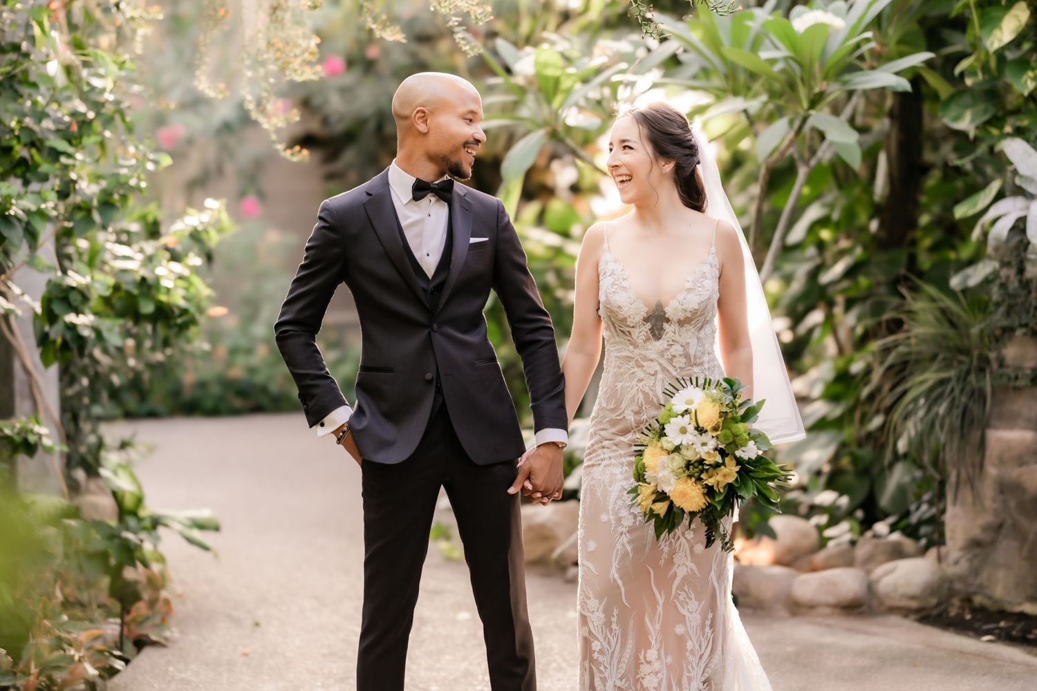 A couple shares a joyful moment in their wedding attire surrounded by lush greenery in a garden setting.