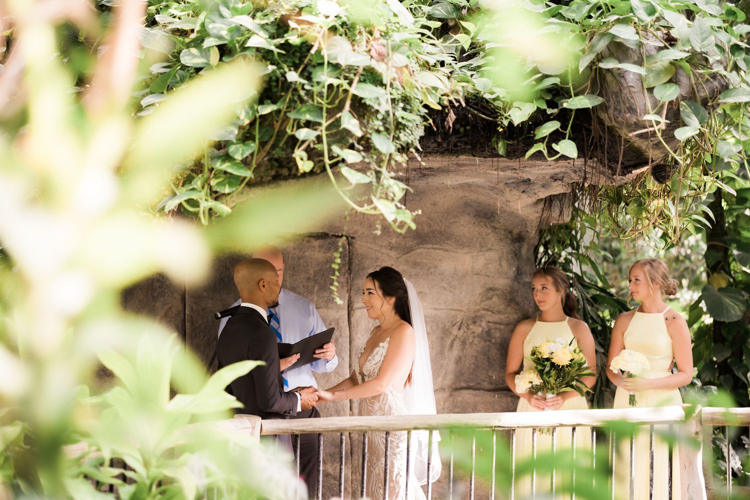 Garden wedding ceremony with guests and bridal party on stone balcony.