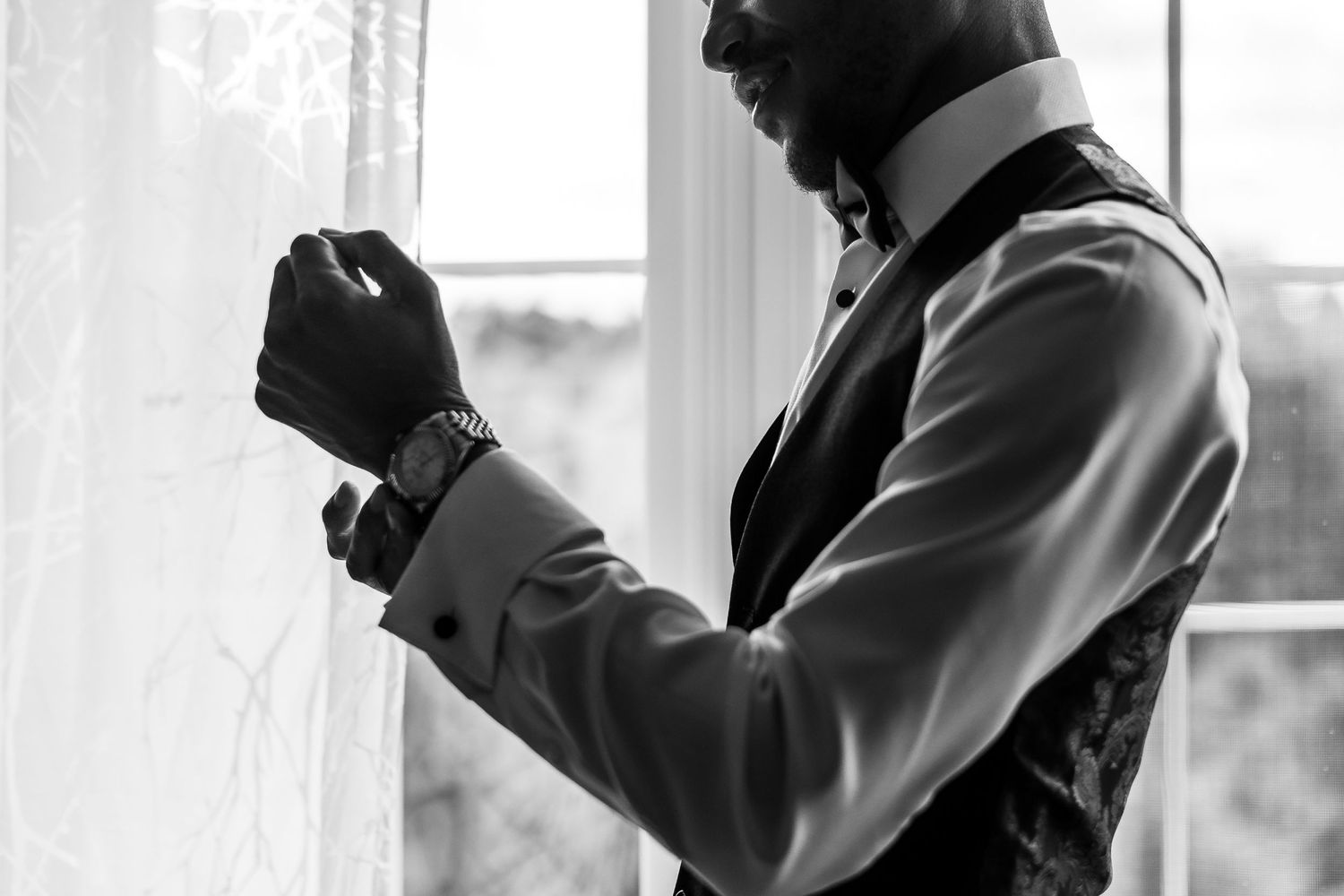 Black and white profile silhouette of someone adjusting formal wear near a window.