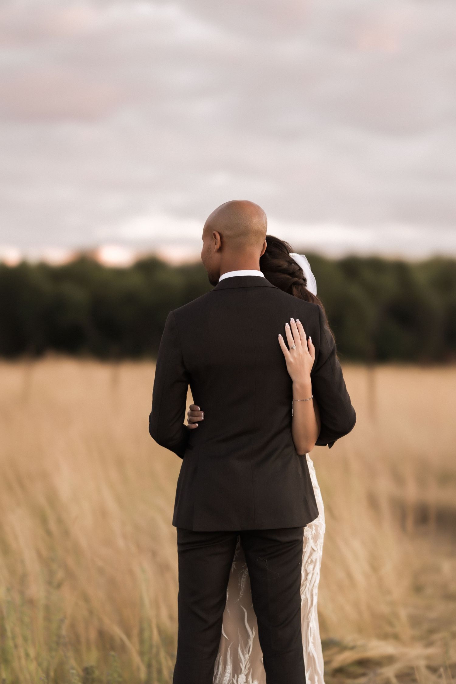 Couple embracing in a golden field with sunset sky behind them.