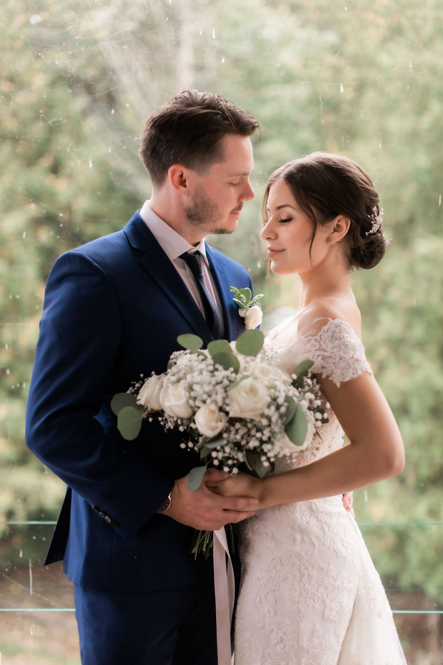 Romantic wedding portrait with couple holding white flower bouquet in natural setting.