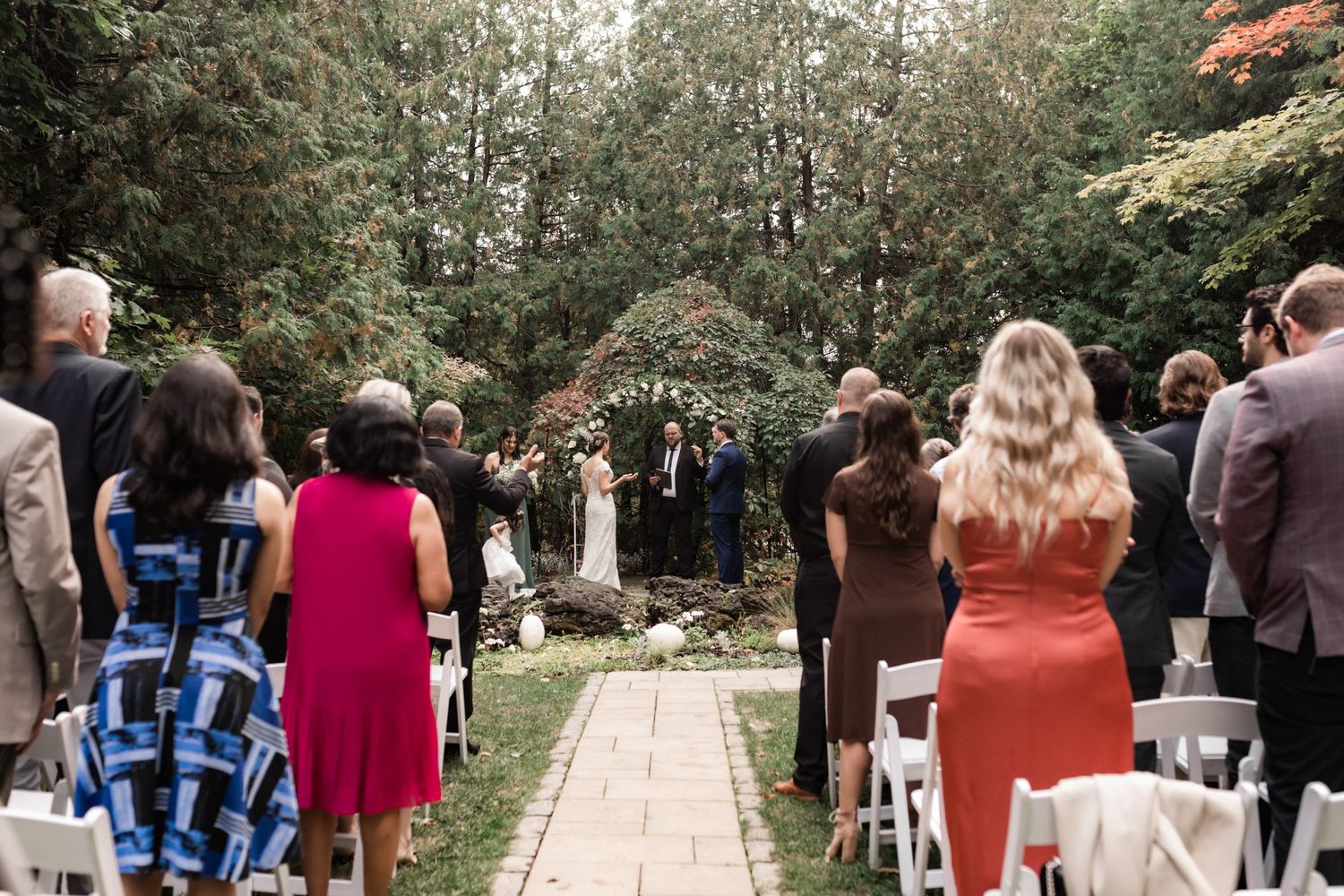 Wedding ceremony setup with stone pathway and white chairs surrounded by lush greenery.