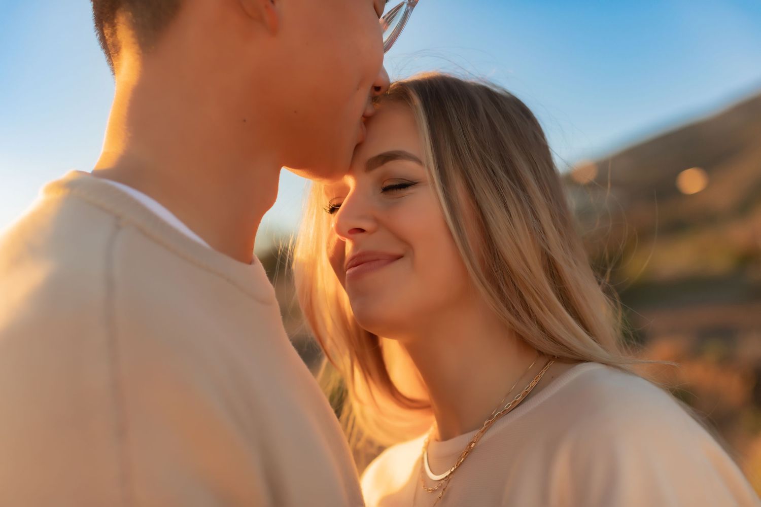 Intimate close-up of couple sharing romantic moment on clifftop during sunset.