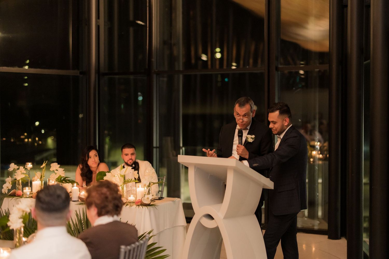 Wedding reception speech being delivered at an elegant evening venue with guests seated.