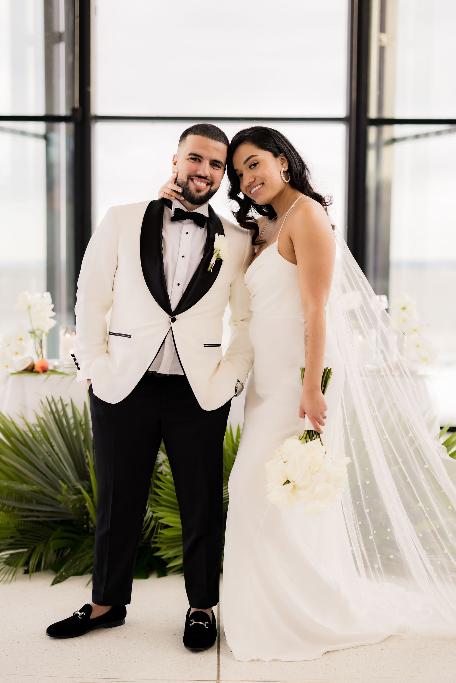 Wedding couple poses together in modern venue with floor-to-ceiling windows.