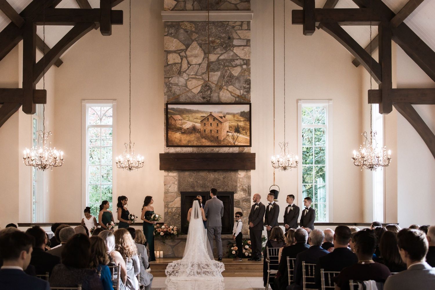 Wedding ceremony in elegant chapel with stone fireplace and hanging chandeliers.