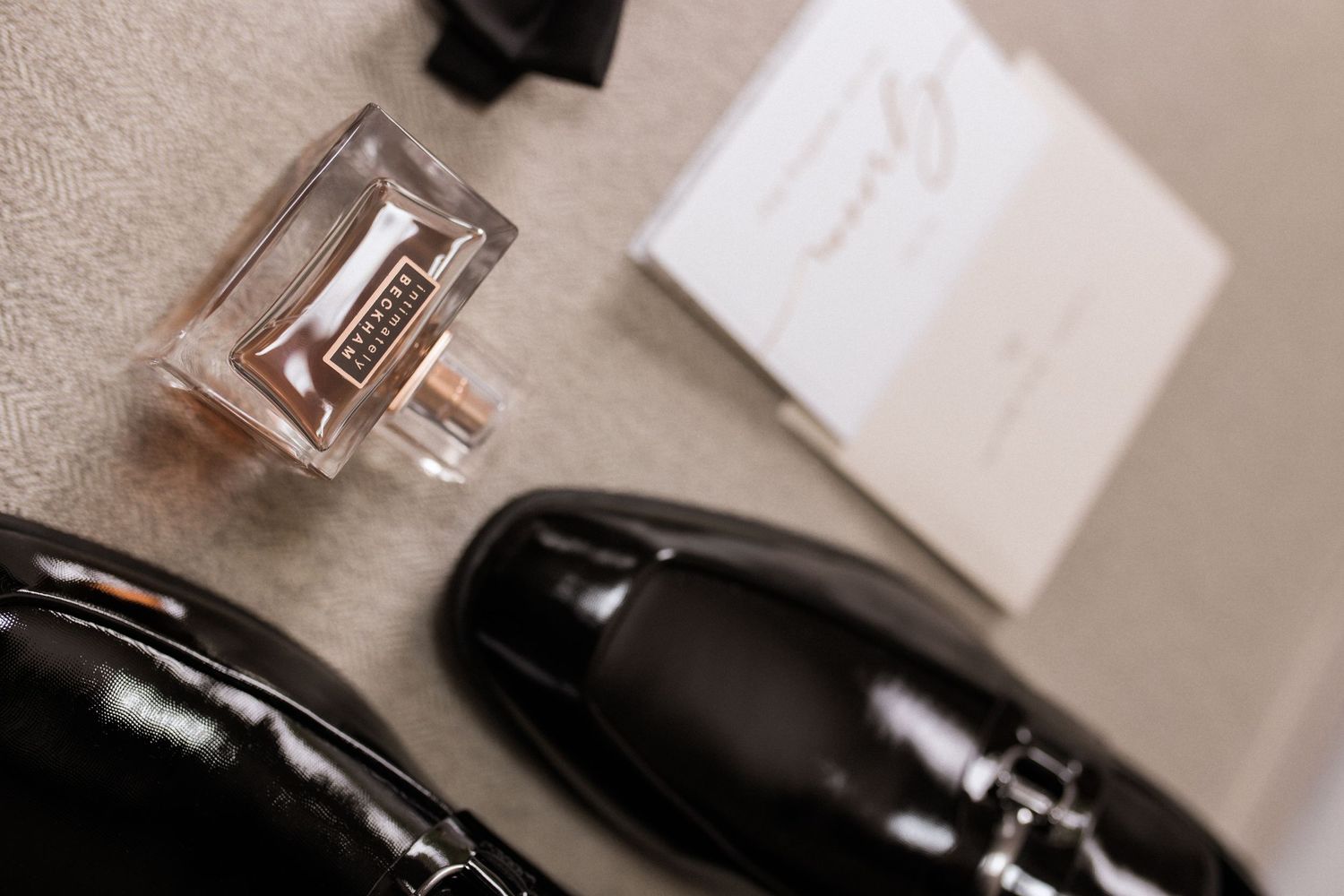 Elegant black dress shoes with cologne bottle and white note card on neutral background.