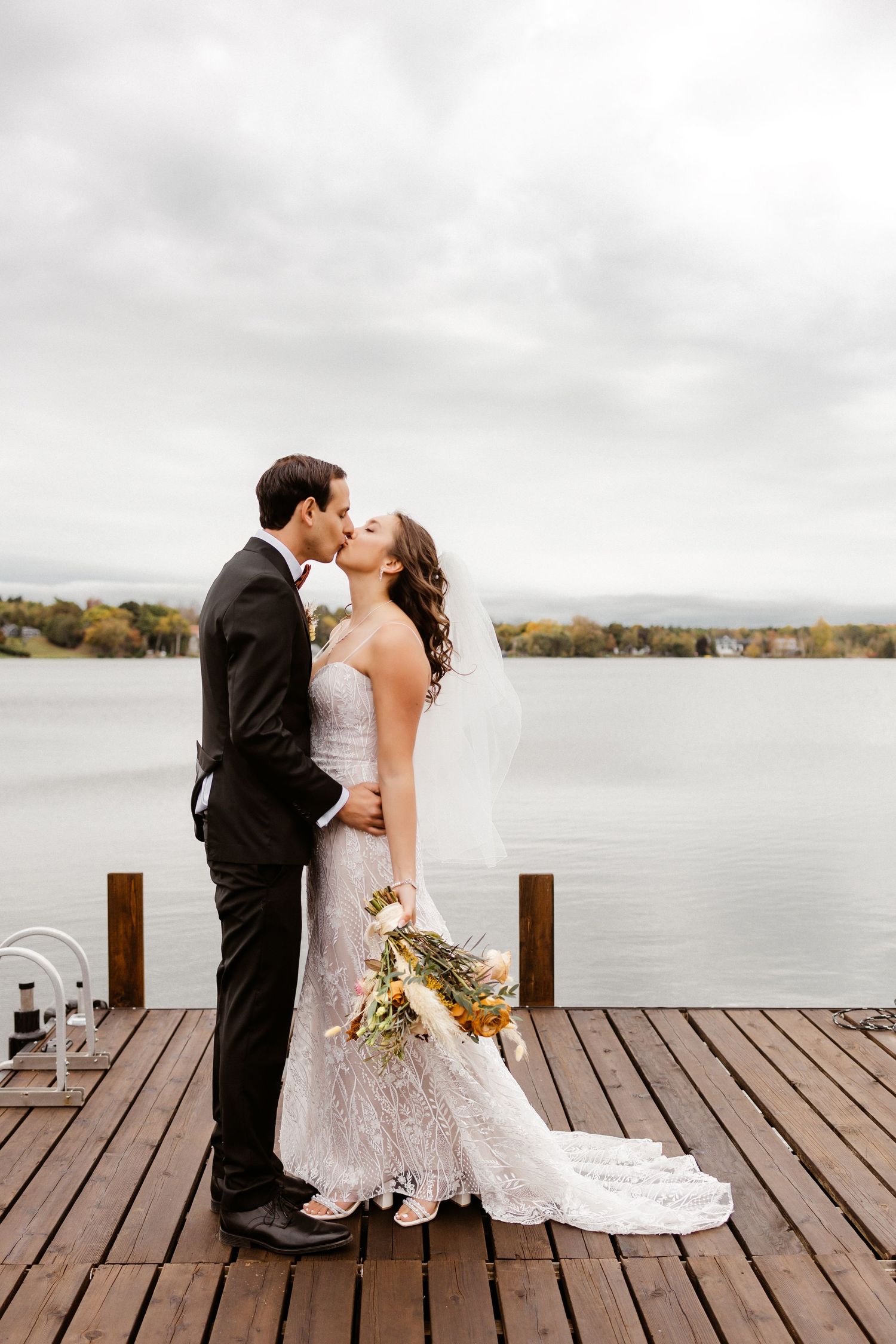 A romantic wedding portrait on a wooden dock overlooking a serene lake.