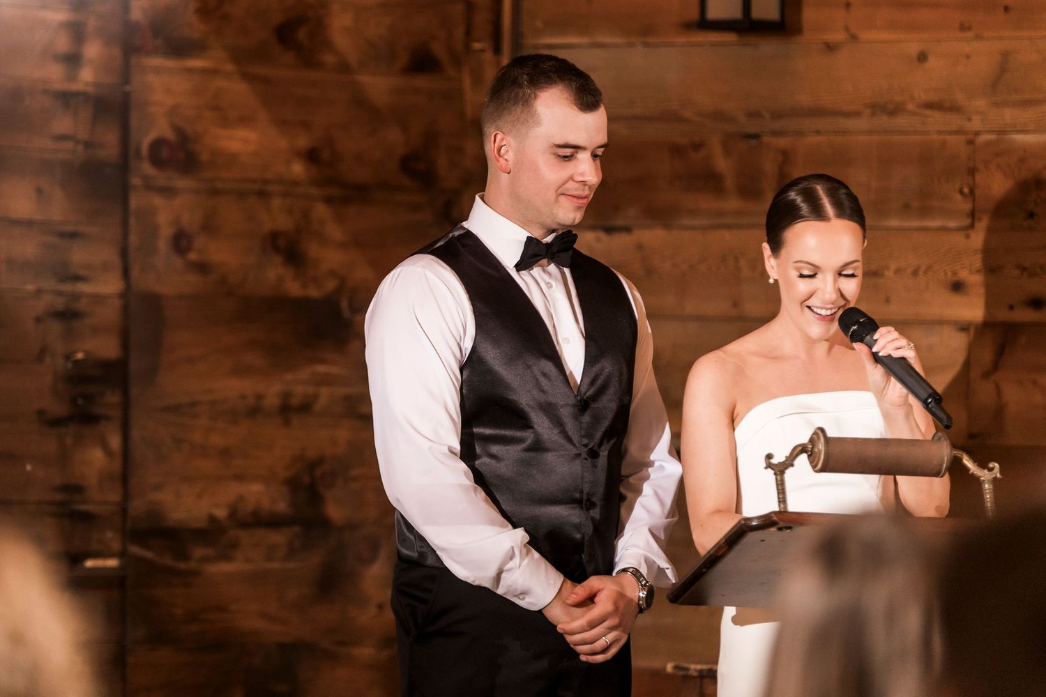 Two people sharing a tender moment during a wedding reception in a rustic barn venue with warm wooden walls.