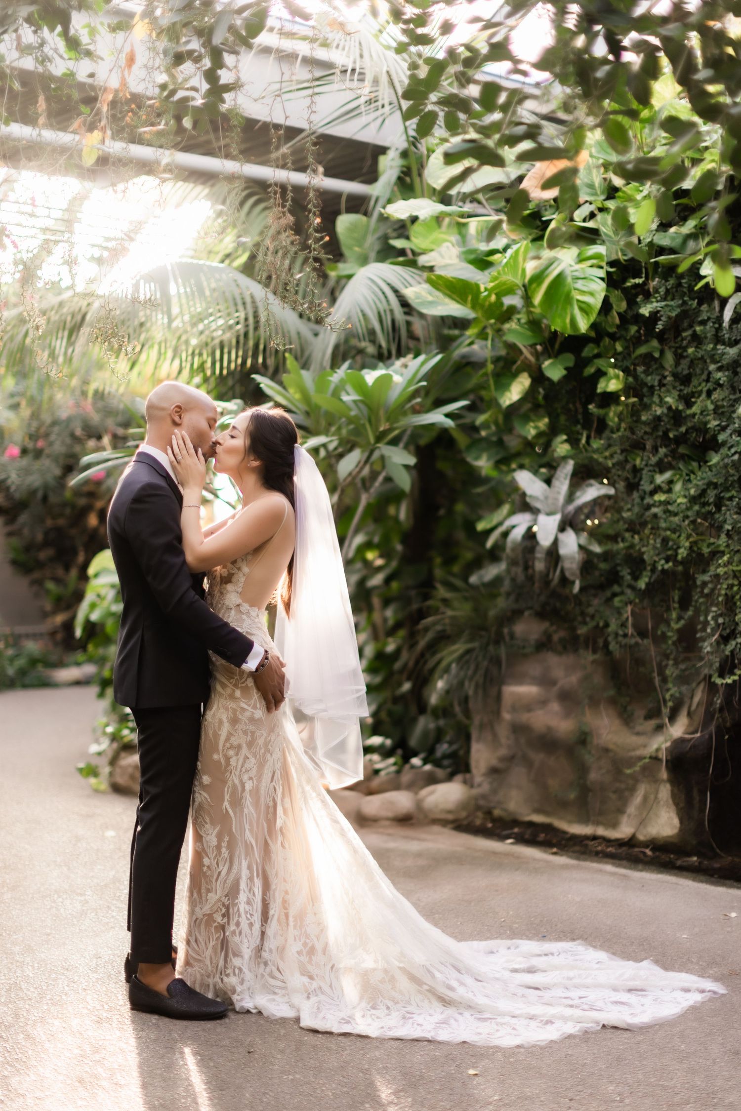 Elegant wedding couple poses on garden path surrounded by lush greenery.
