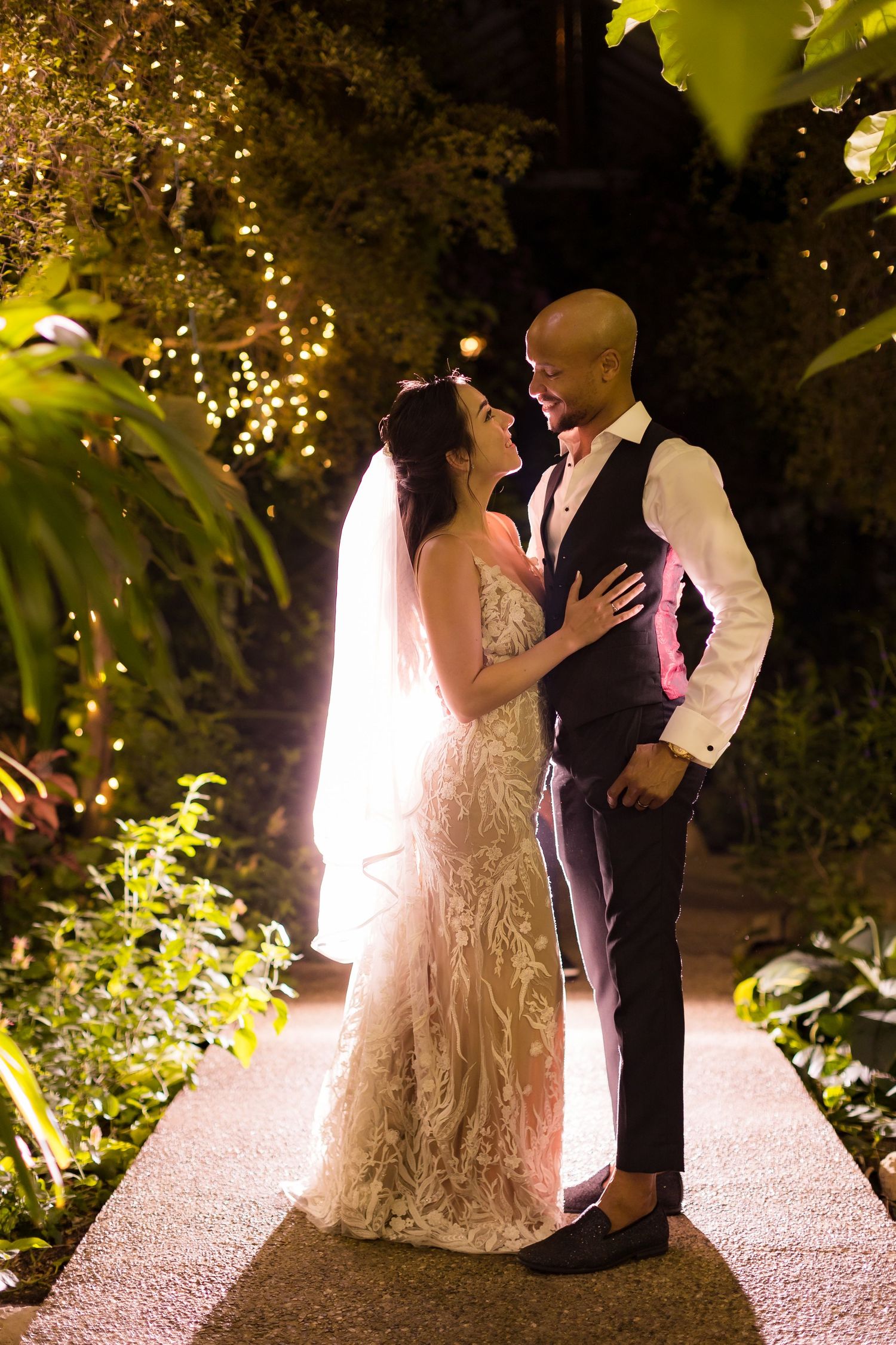 Intimate portrait of newlyweds on illuminated garden path with twinkling lights.