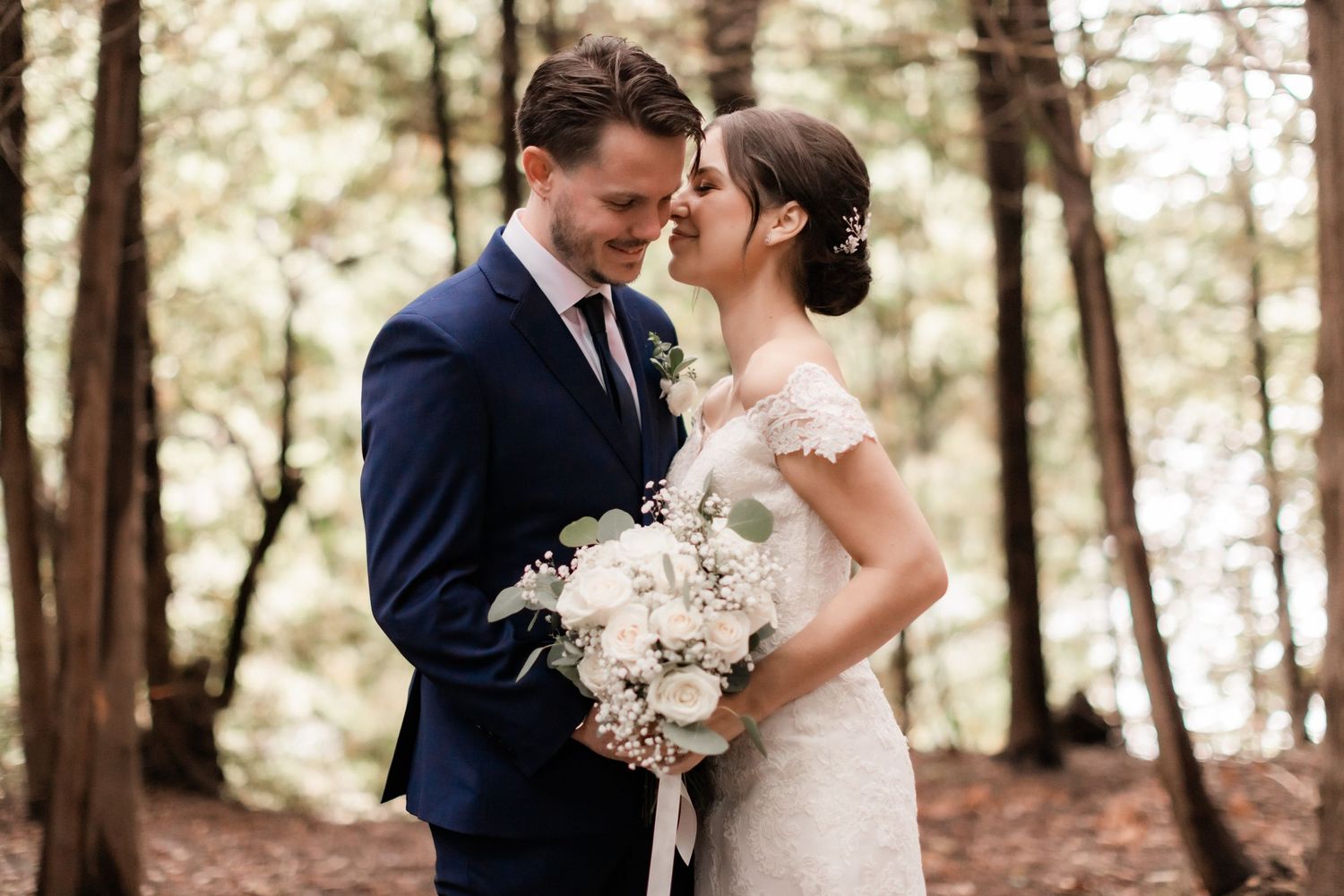 Intimate forest wedding portrait with couple sharing romantic moment among trees.