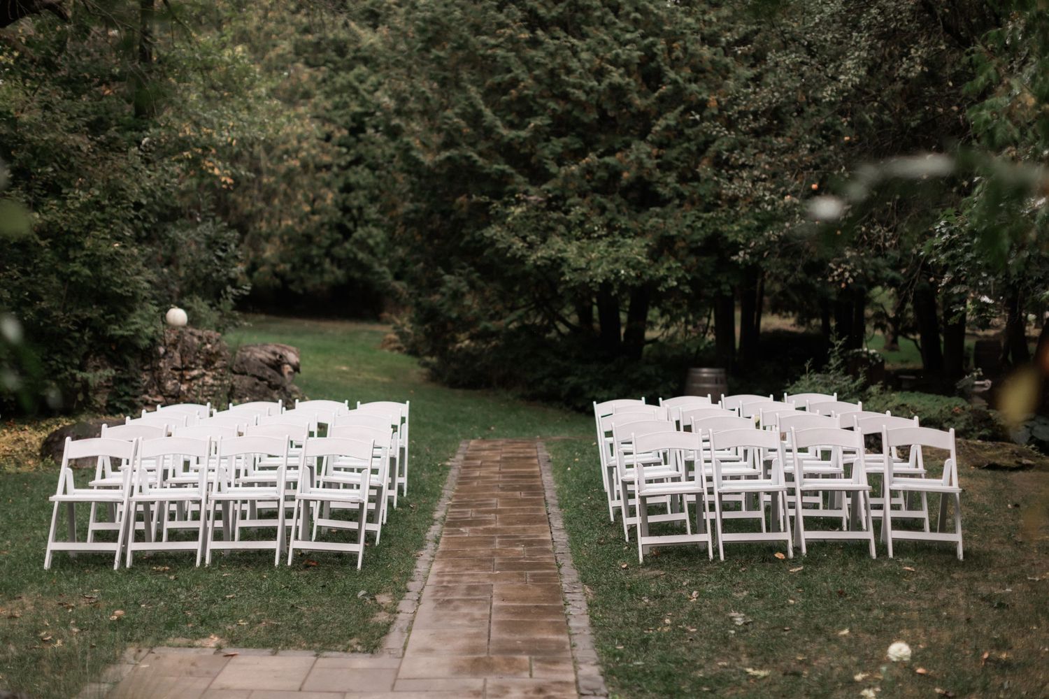 White wooden chairs arranged in rows for an outdoor woodland wedding ceremony.