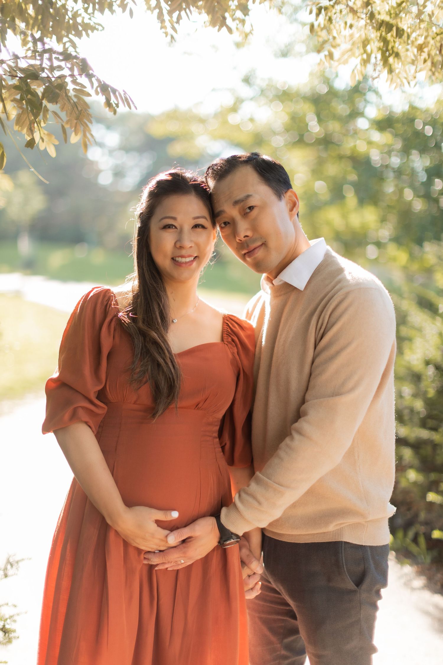 Sun-drenched maternity portrait of couple in coordinating earth tones against natural backdrop.